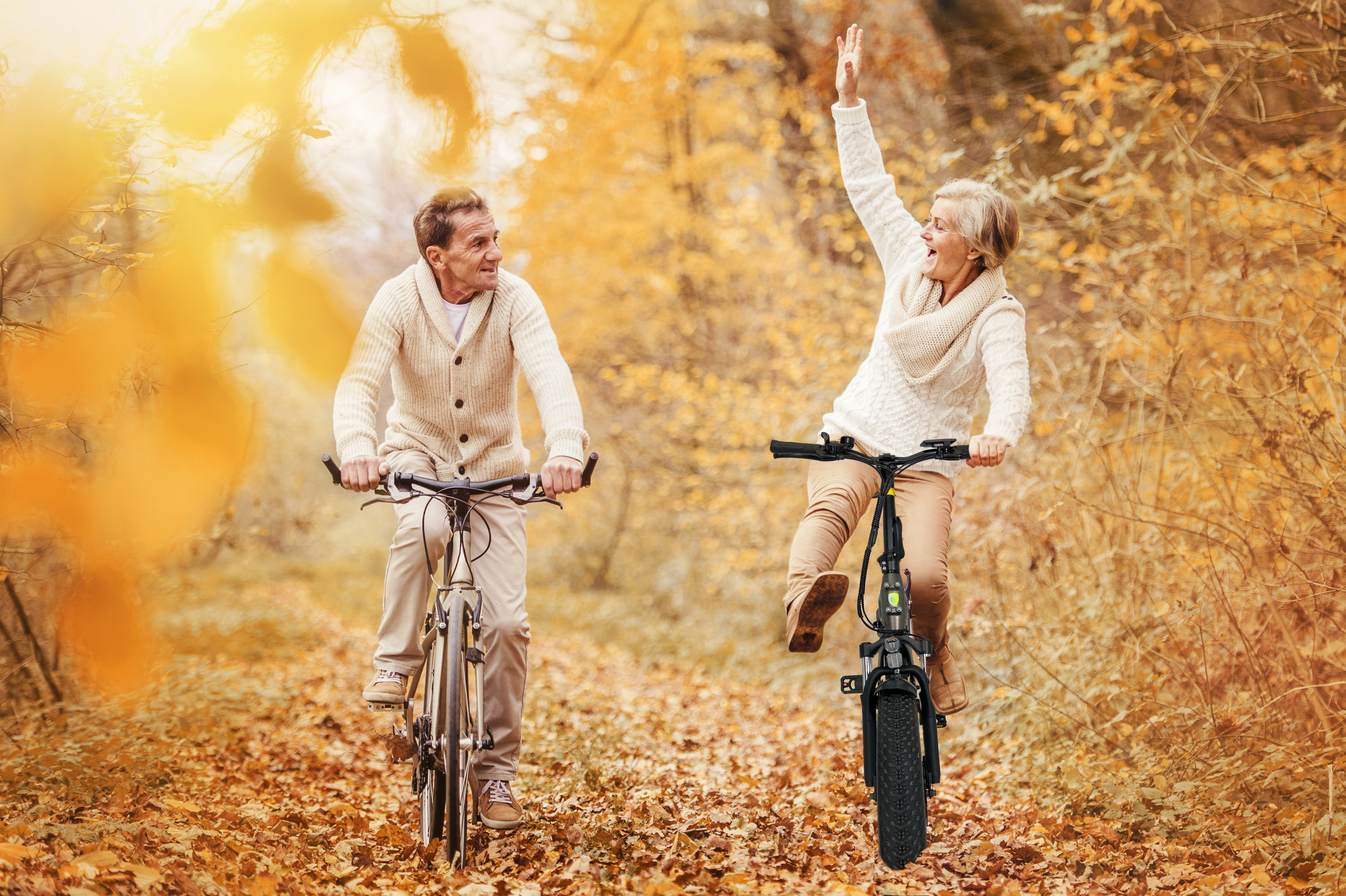 Zwei Personen auf Fahrrädern im Herbst. Einer hebt den Arm, der andere lächelt.