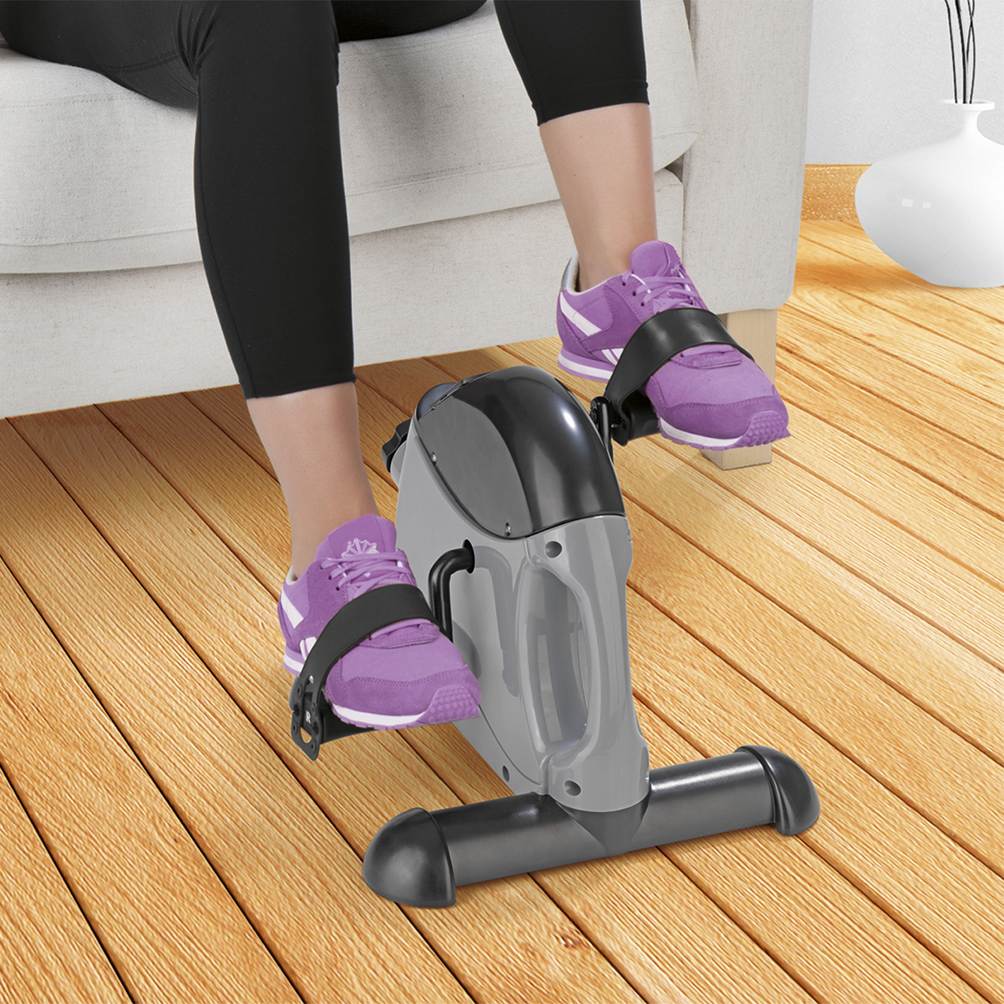 Person benutzt ein Mini-Heimtrainer. Person trägt lila Turnschuhe und schwarze Leggings. Holzboden.