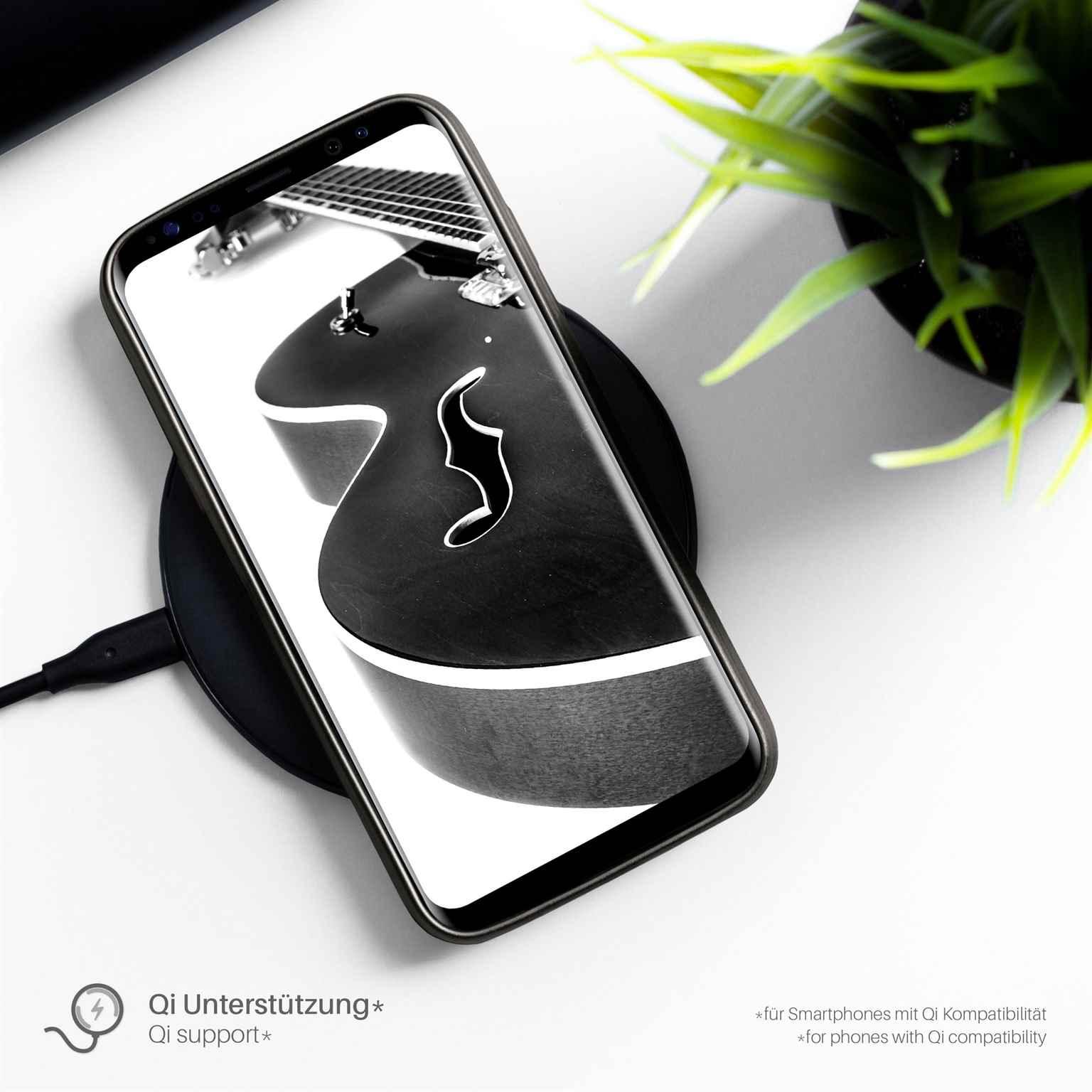 Telefon auf kabellosem Ladegerät. Gitarrenbild auf dem Bildschirm. Schwarze Oberfläche. Grüne Pflanze.