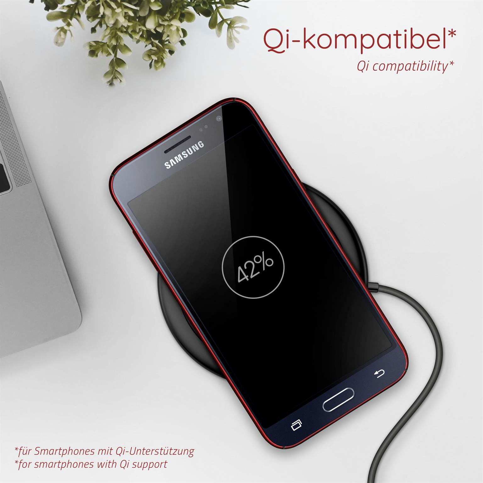Ein Telefon lädt auf einem schwarzen Pad. Bildschirm zeigt 42%. Pflanze links.