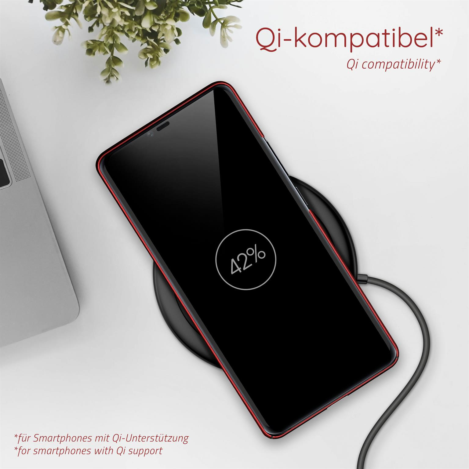 Telefon auf Ladegerät, lädt 42%. Rot umrandetes Telefon, schwarze Basis. Pflanze im Hintergrund.