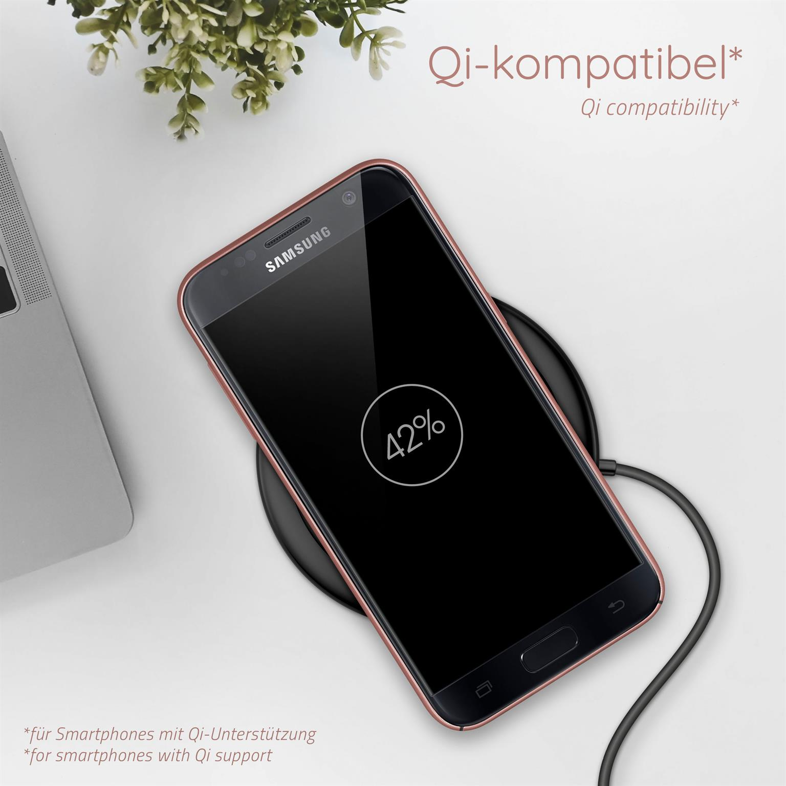 Ein Telefon auf einem kabellosen Ladegerät, das 42% Akku anzeigt. Ein Laptop und eine Pflanze im Hintergrund.