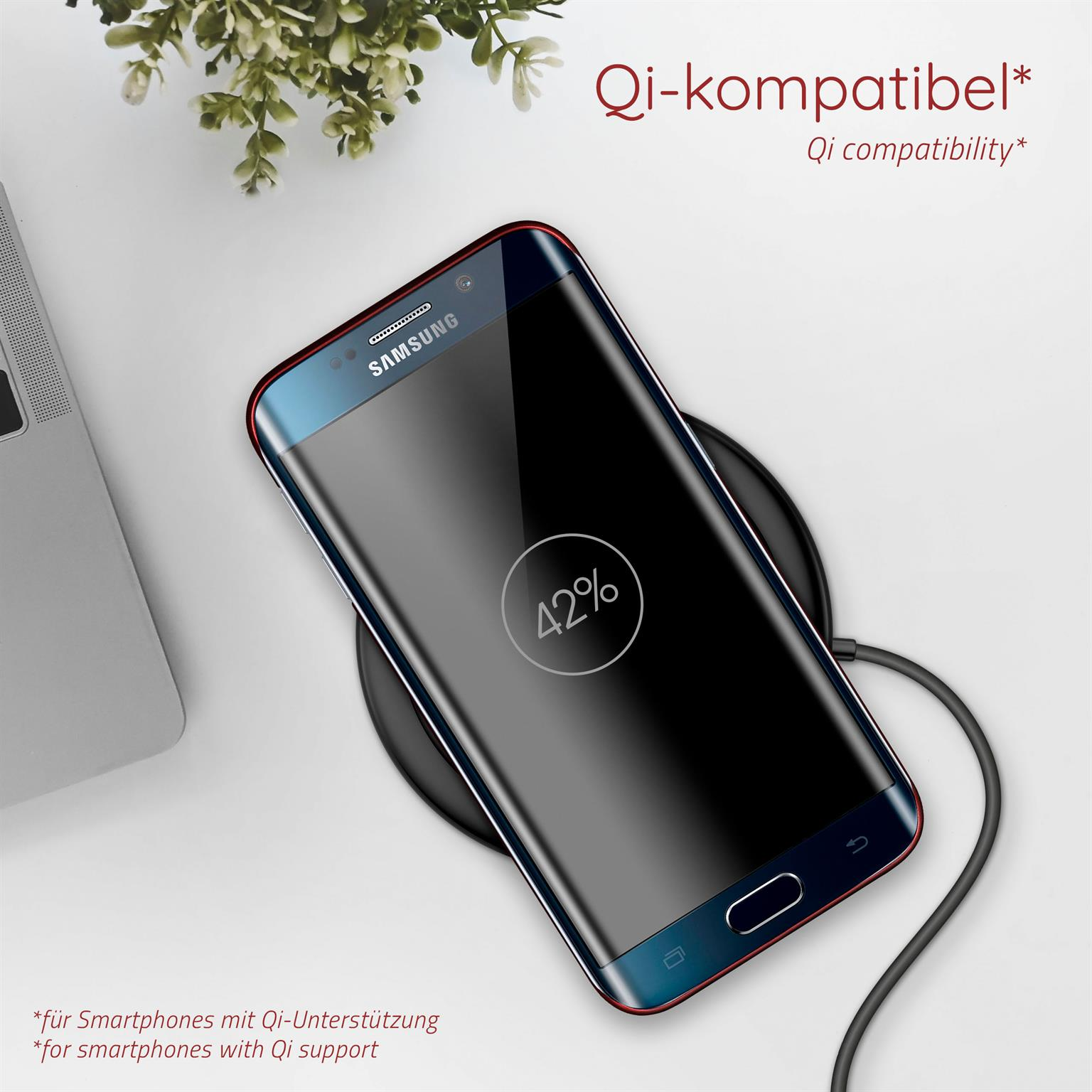 Schwarzes Telefon auf kabellosem Ladegerät. Der Bildschirm zeigt 42% Akku. Eine Pflanze ist im Hintergrund.