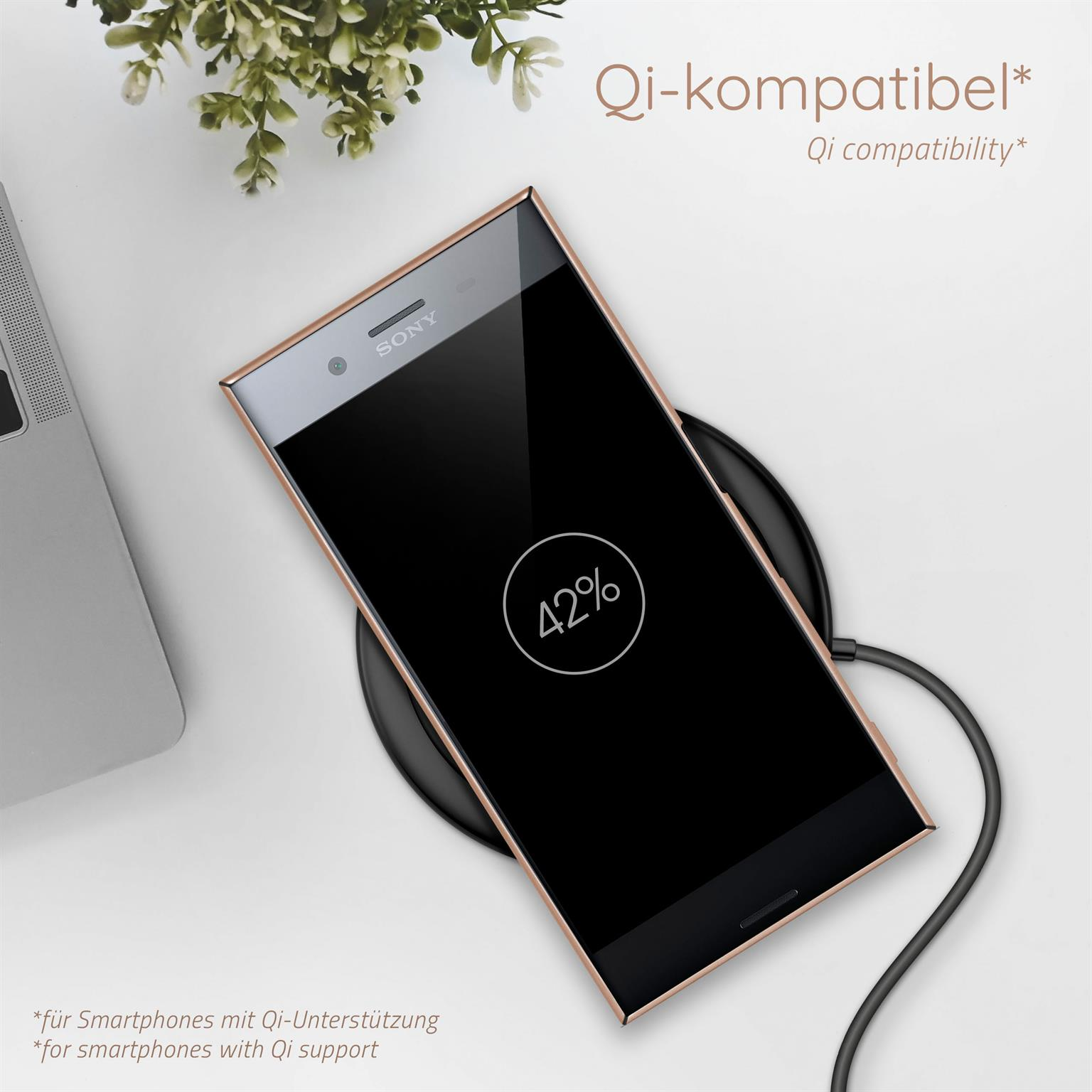 Ein Telefon, das drahtlos geladen wird. Der Bildschirm zeigt 42 %. Im Hintergrund eine Pflanze und ein Laptop.