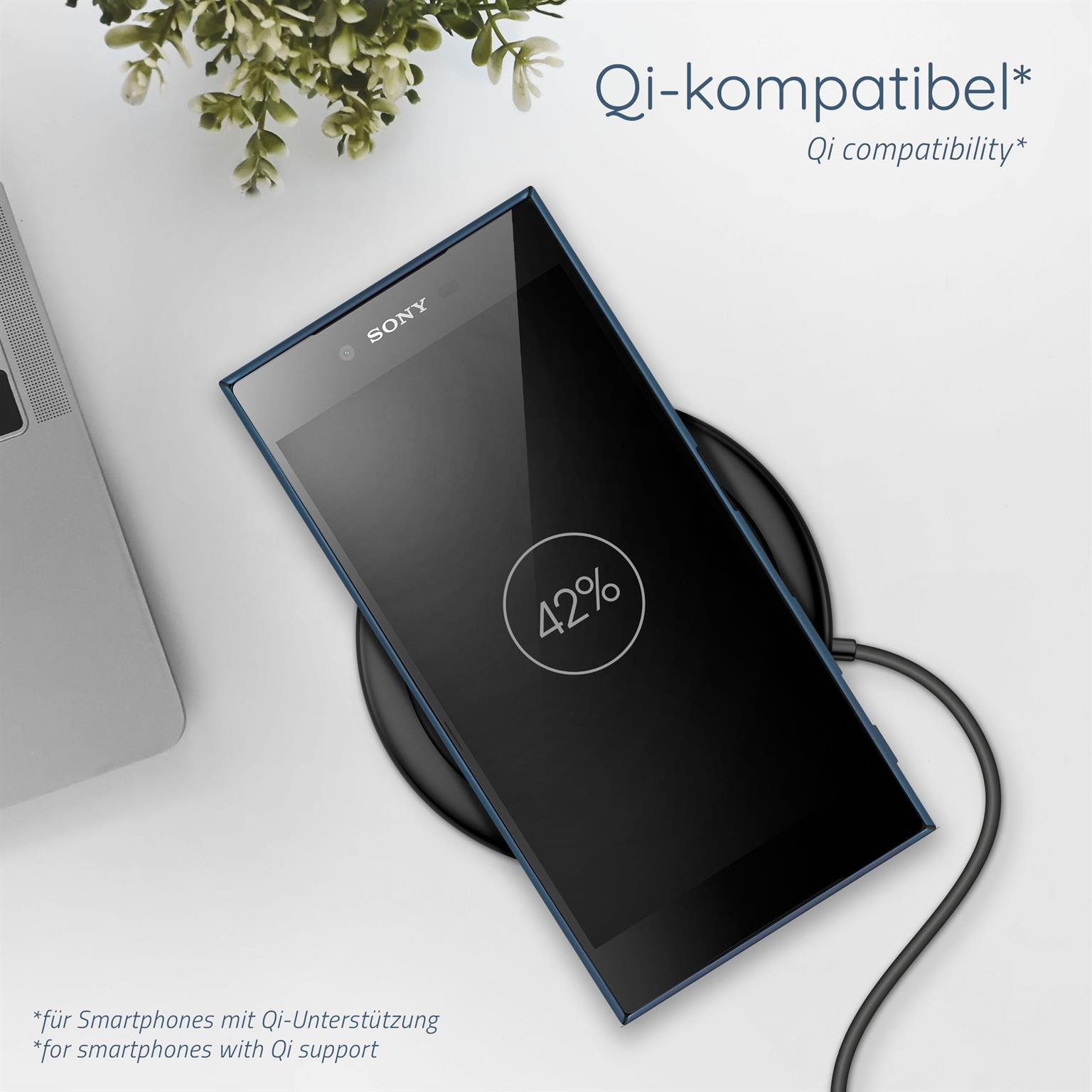 Schwarzes Telefon auf kabellosem Ladegerät. Der Bildschirm zeigt 42% Akku. Eine Pflanze im Hintergrund.