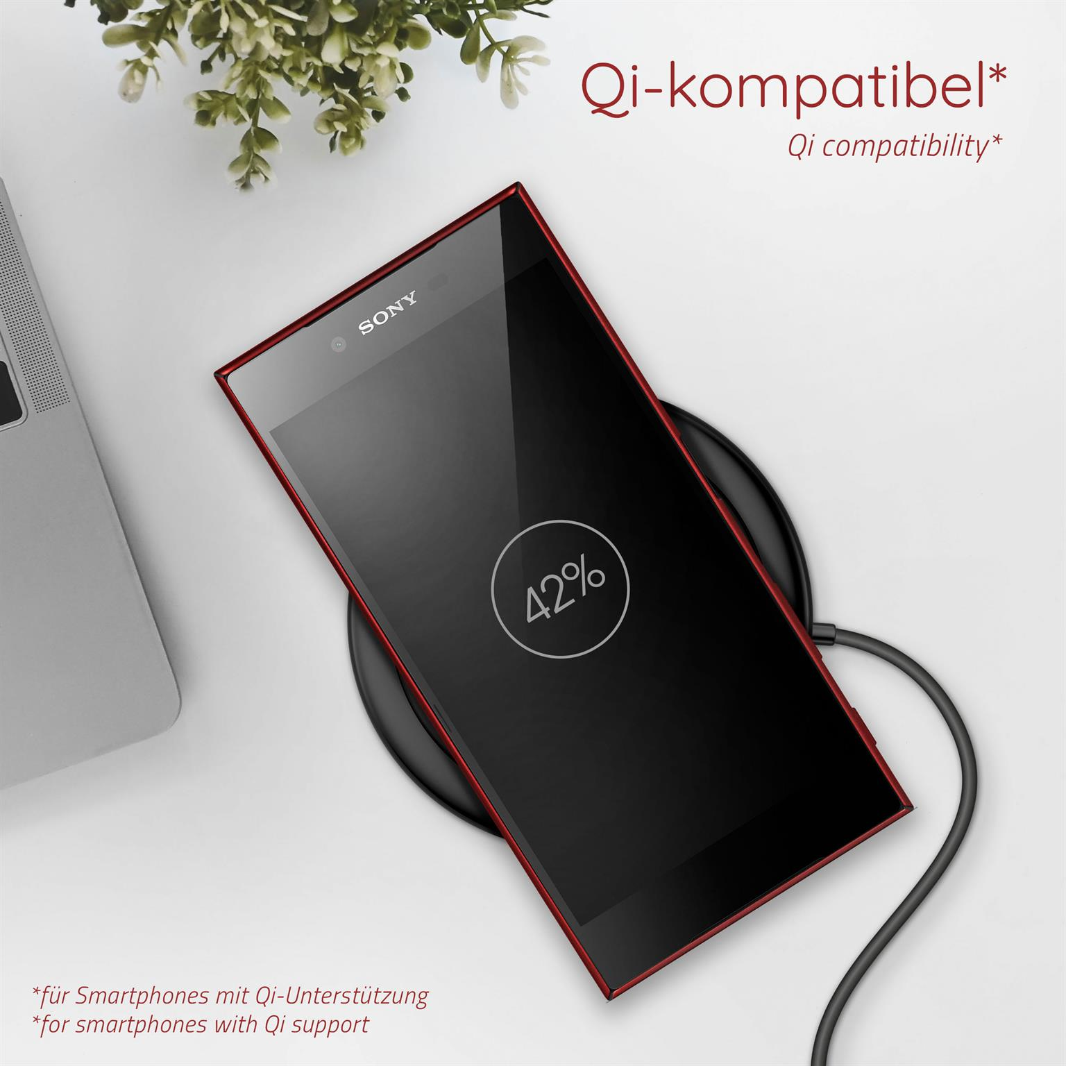 Ein schwarzes Telefon auf einem kabellosen Ladegerät, mit rotem Rand, weißem Hintergrund und einer grünen Pflanze.