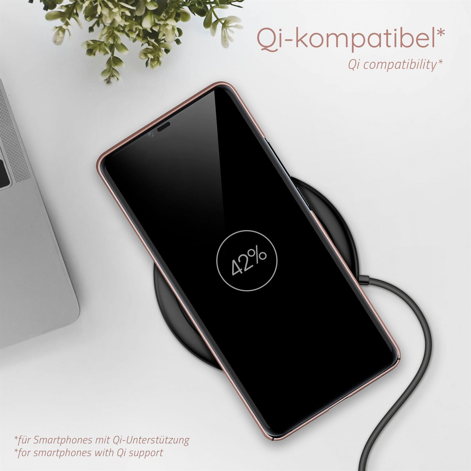 Telefon auf kabellosem Ladegerät. Hintergrund: grüne Pflanzen.