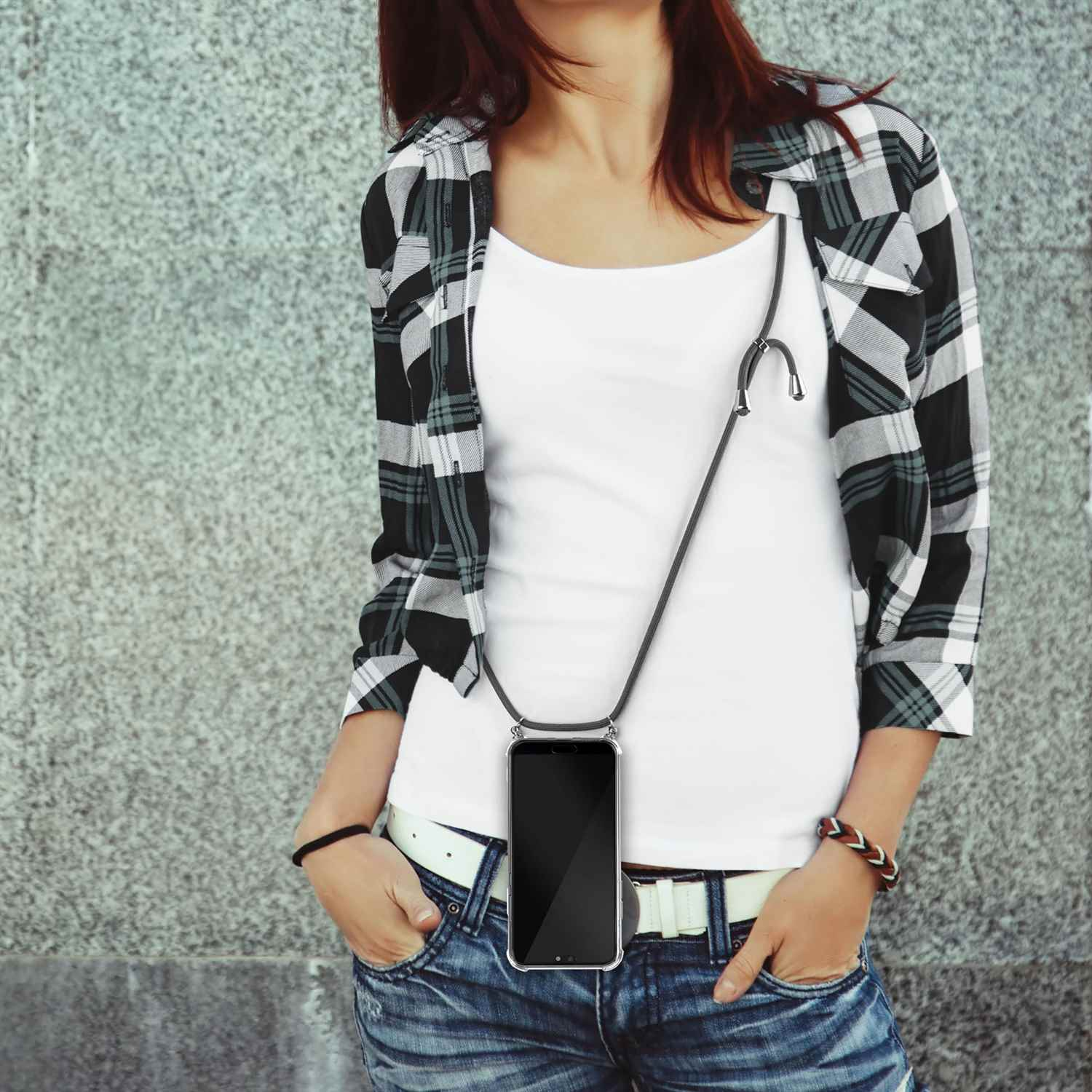 Frau in kariertem Hemd hält Handy mit Umhängeband. Weißes Shirt und schwarze Hose.