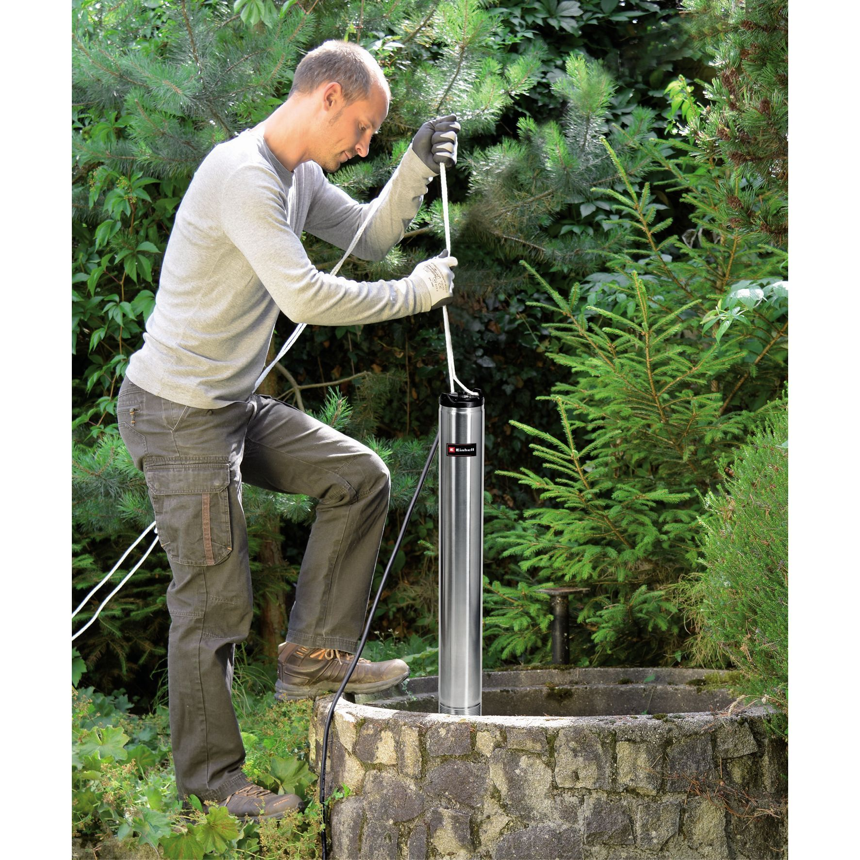 Ein Mann in einem Garten verwendet eine Pumpe, um Wasser aus einem Brunnen zu ziehen.