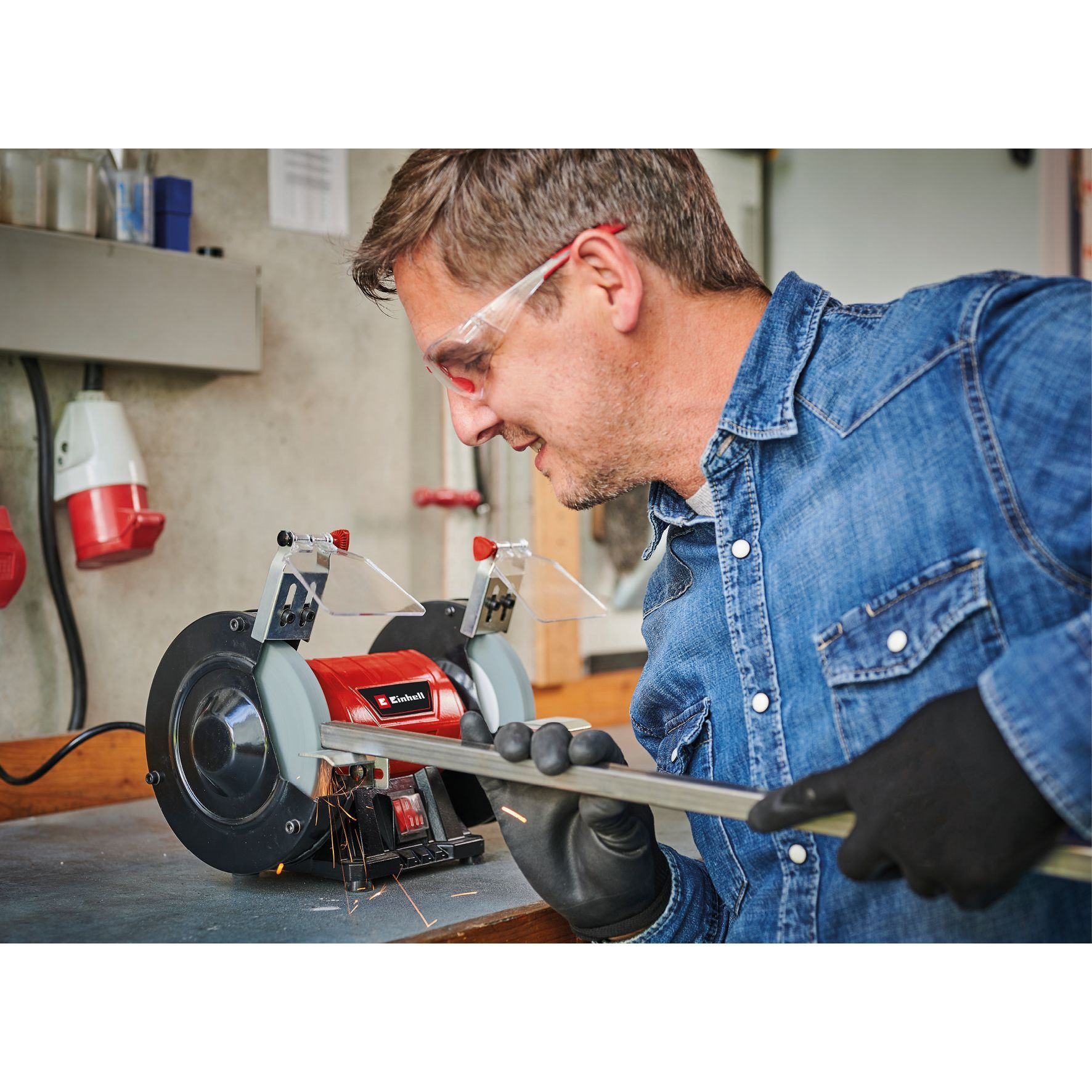 Hombre con gafas de seguridad esmerila metal con una amoladora roja. Se ven chispas.