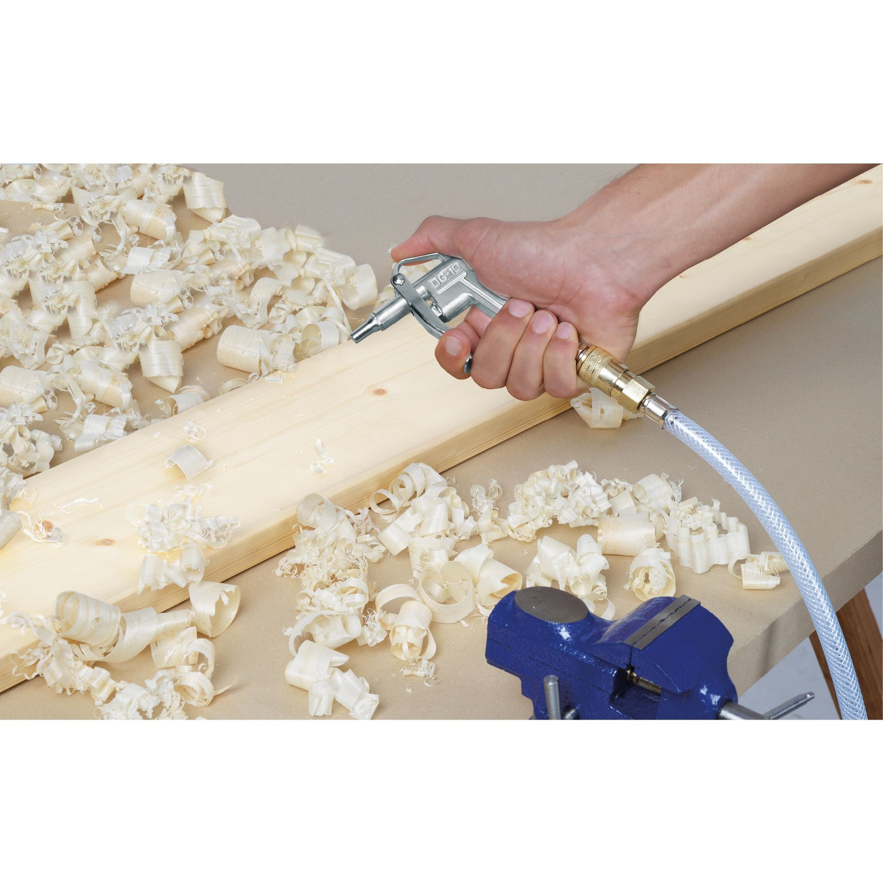 Mano che tiene l'ugello dell'aria, trucioli di legno sullo sfondo, asse di legno e morsa blu.