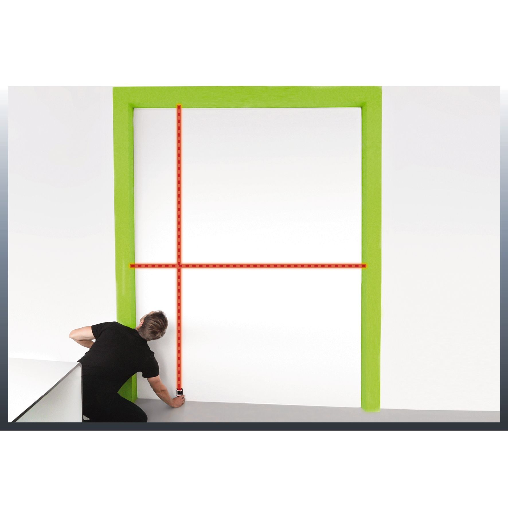 Osoba mierzy zieloną ościeżnicę czerwoną miarką na białej ścianie.