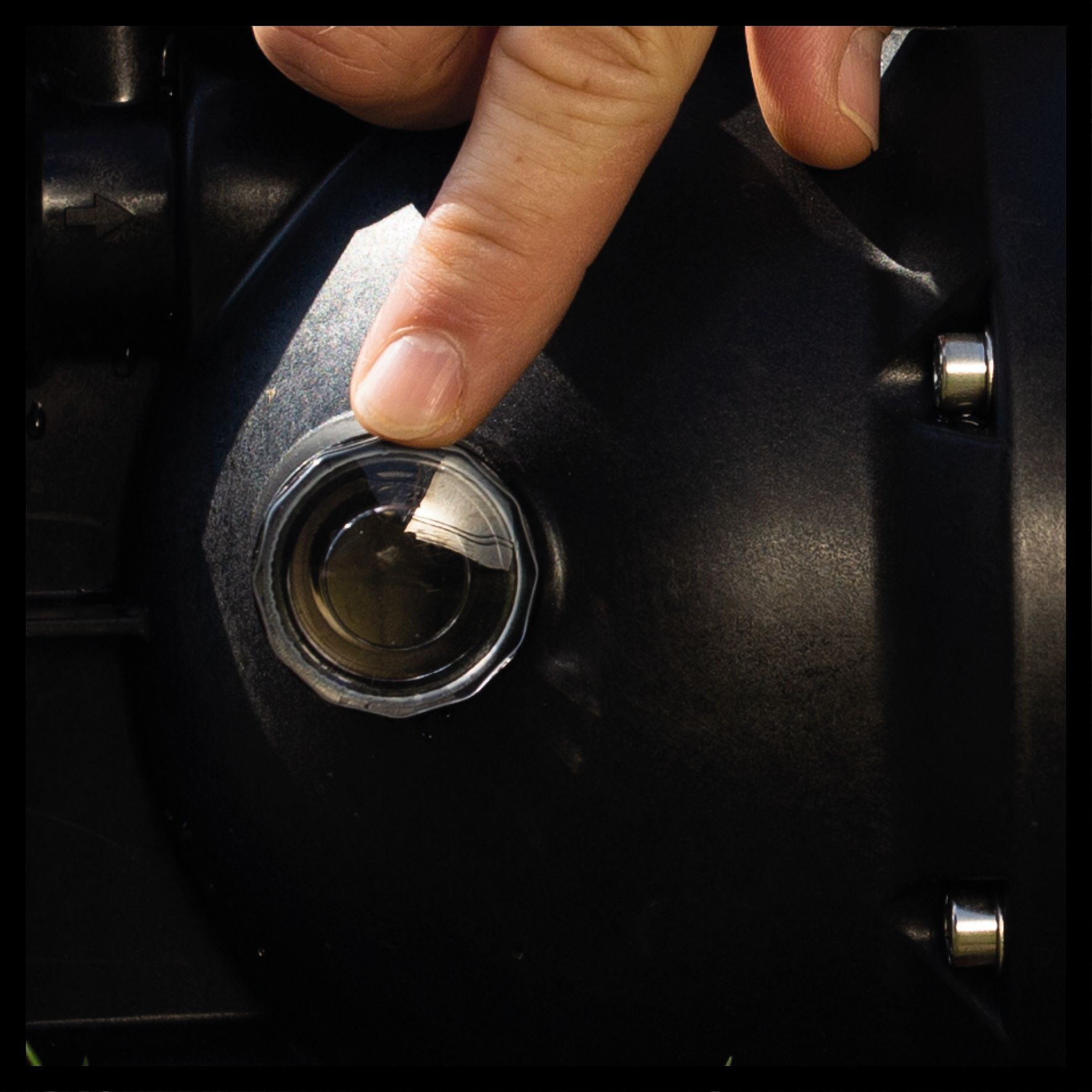 Palec naciska przezroczysty przycisk na czarnym urządzeniu. Dwa srebrne wkręty są z boku.