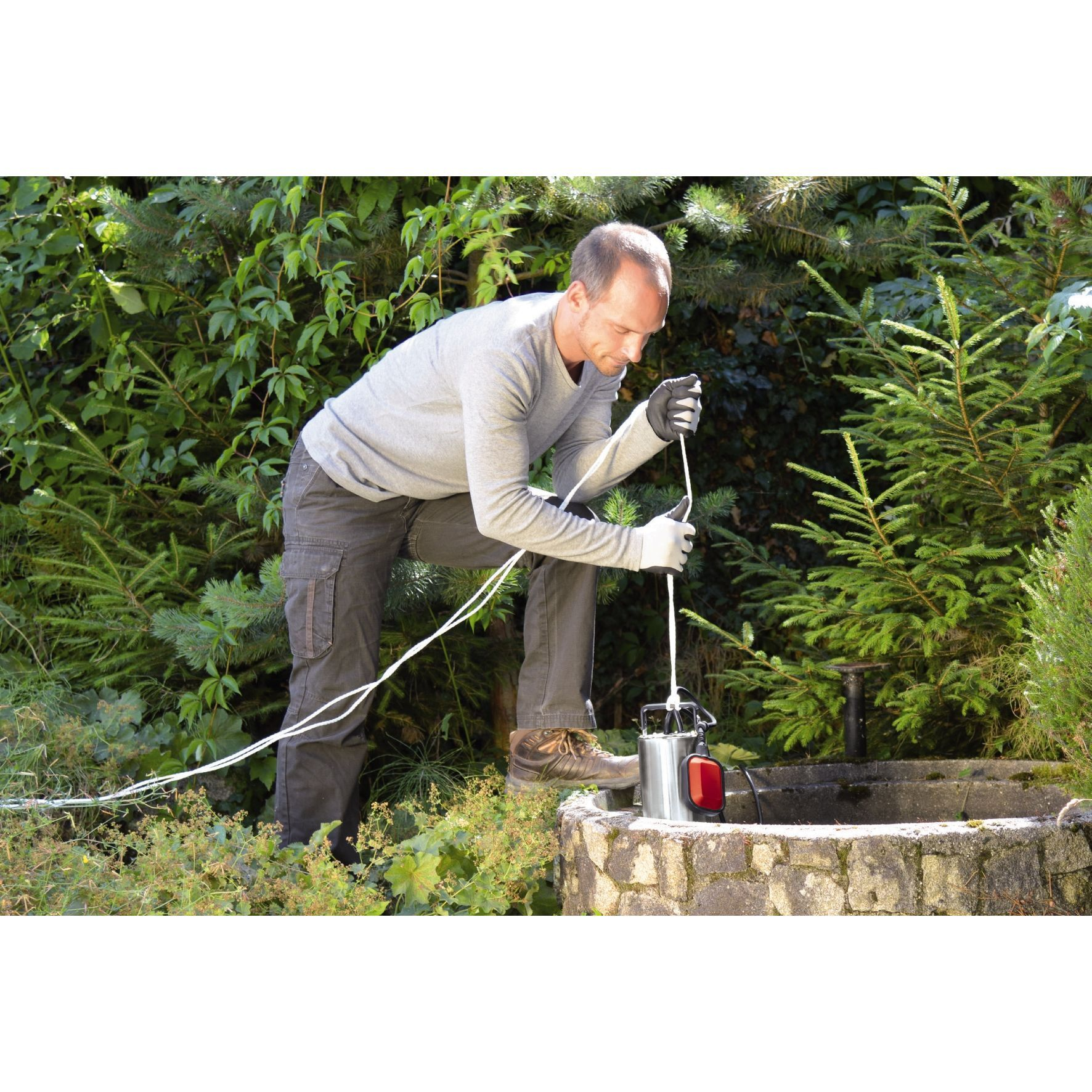 Mężczyzna w szarej koszuli i ciemnych spodniach wyciąga białą linę ze studni.