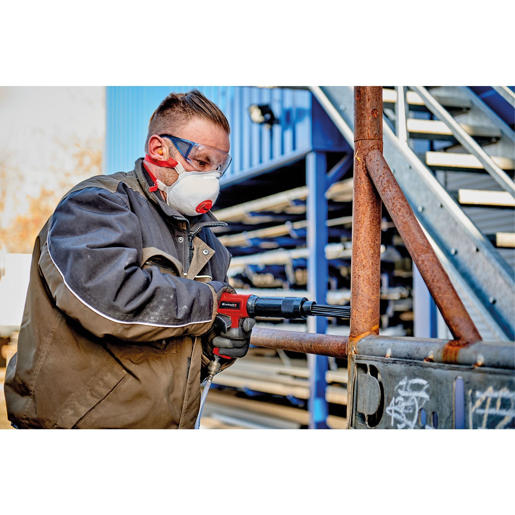 Hombre usando martillo neumático en estructura metálica. Con máscara y gafas.