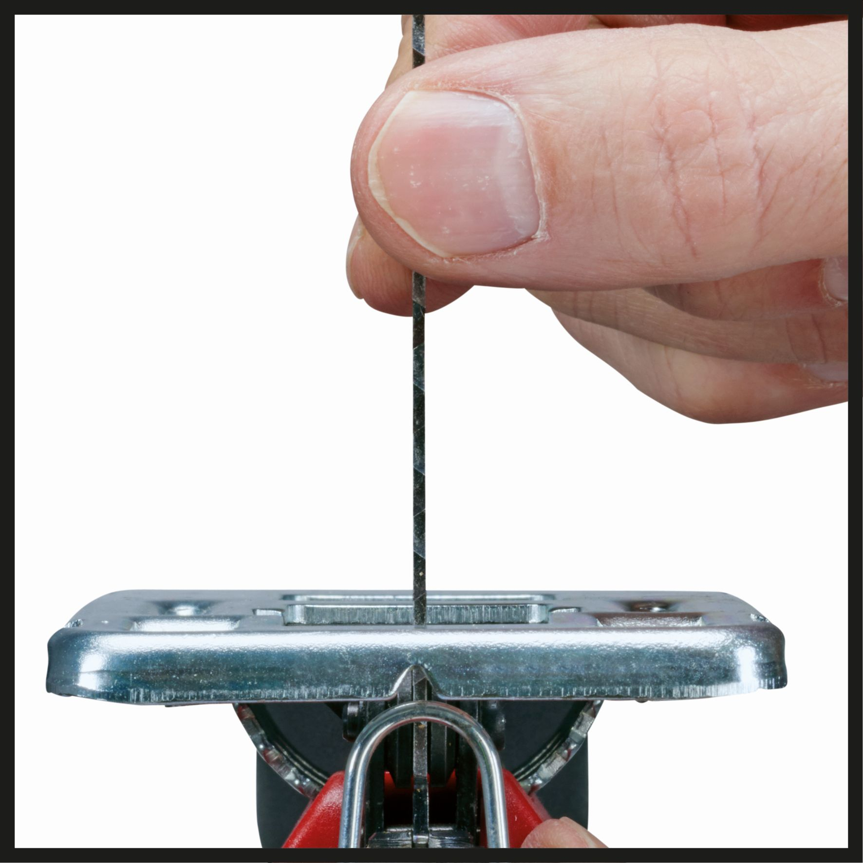 Dłoń trzymająca ostrze wyrzynarki, włożone do metalowego narzędzia. Białe tło.