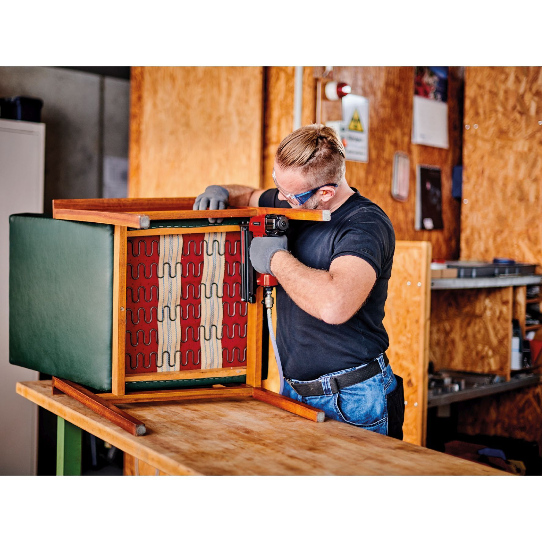 Ein Mann repariert mit einer Tackermaschine einen grünen und Holzstuhl.