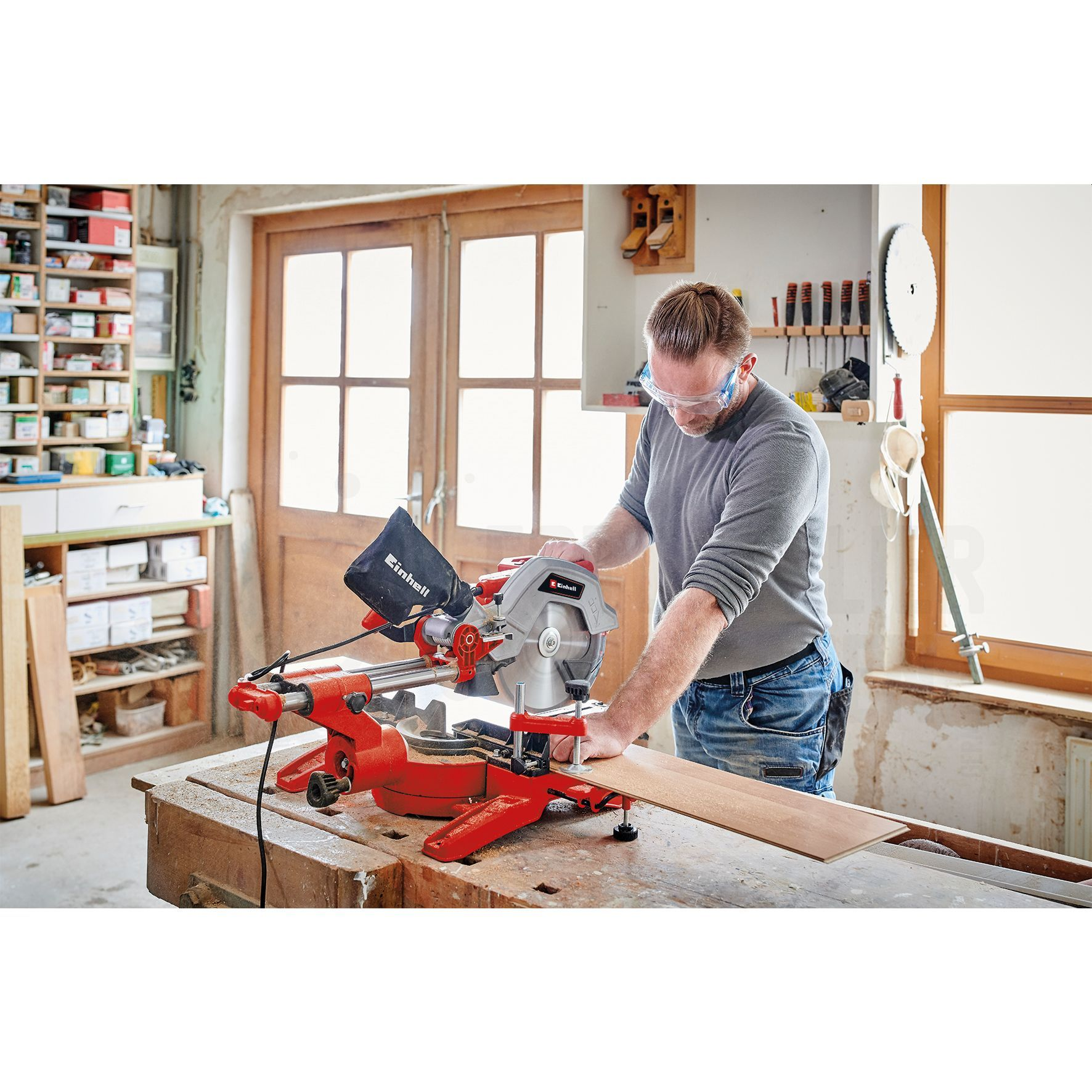 Ein Mann mit Brille schneidet Holz mit einer rot-grauen Säge in einer Werkstatt.