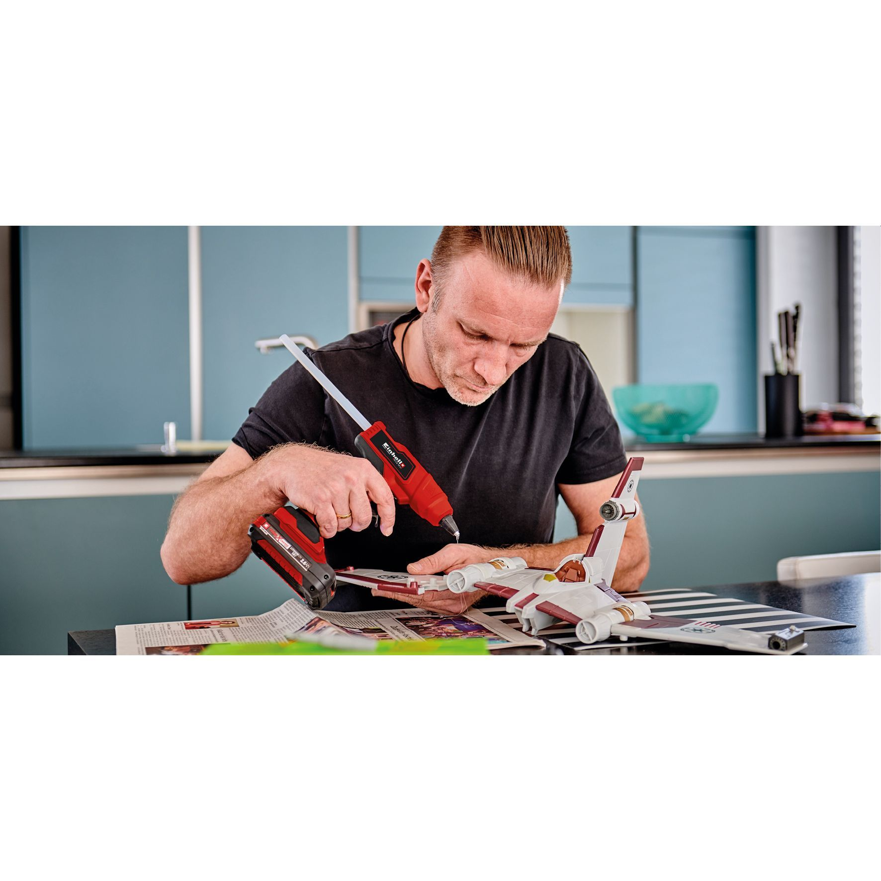 Mężczyzna używa czerwonego pistoletu do klejenia, składając model Star Wars.