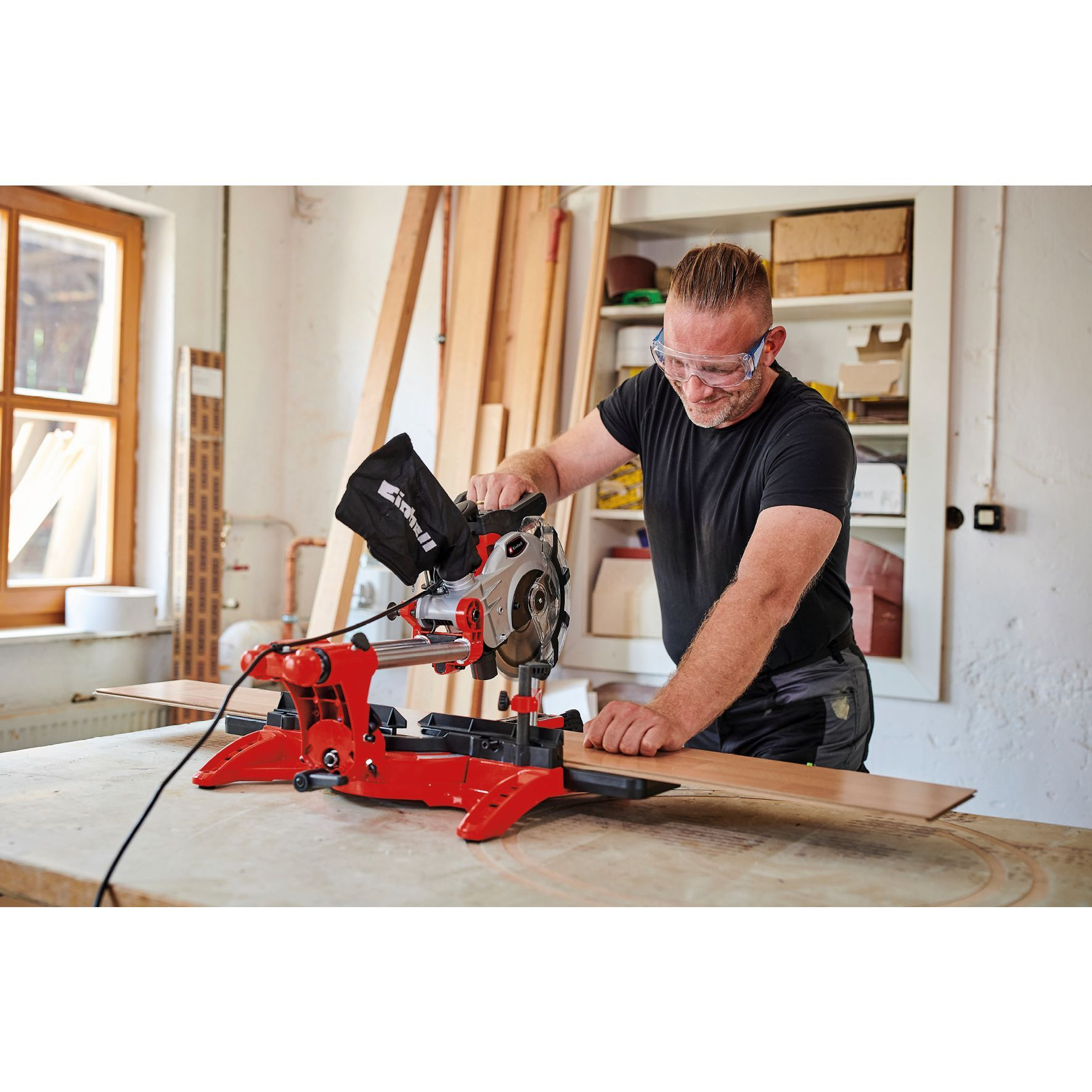 Ein Mann schneidet ein Holzstück mit einer roten Säge. Er trägt eine Schutzbrille.
