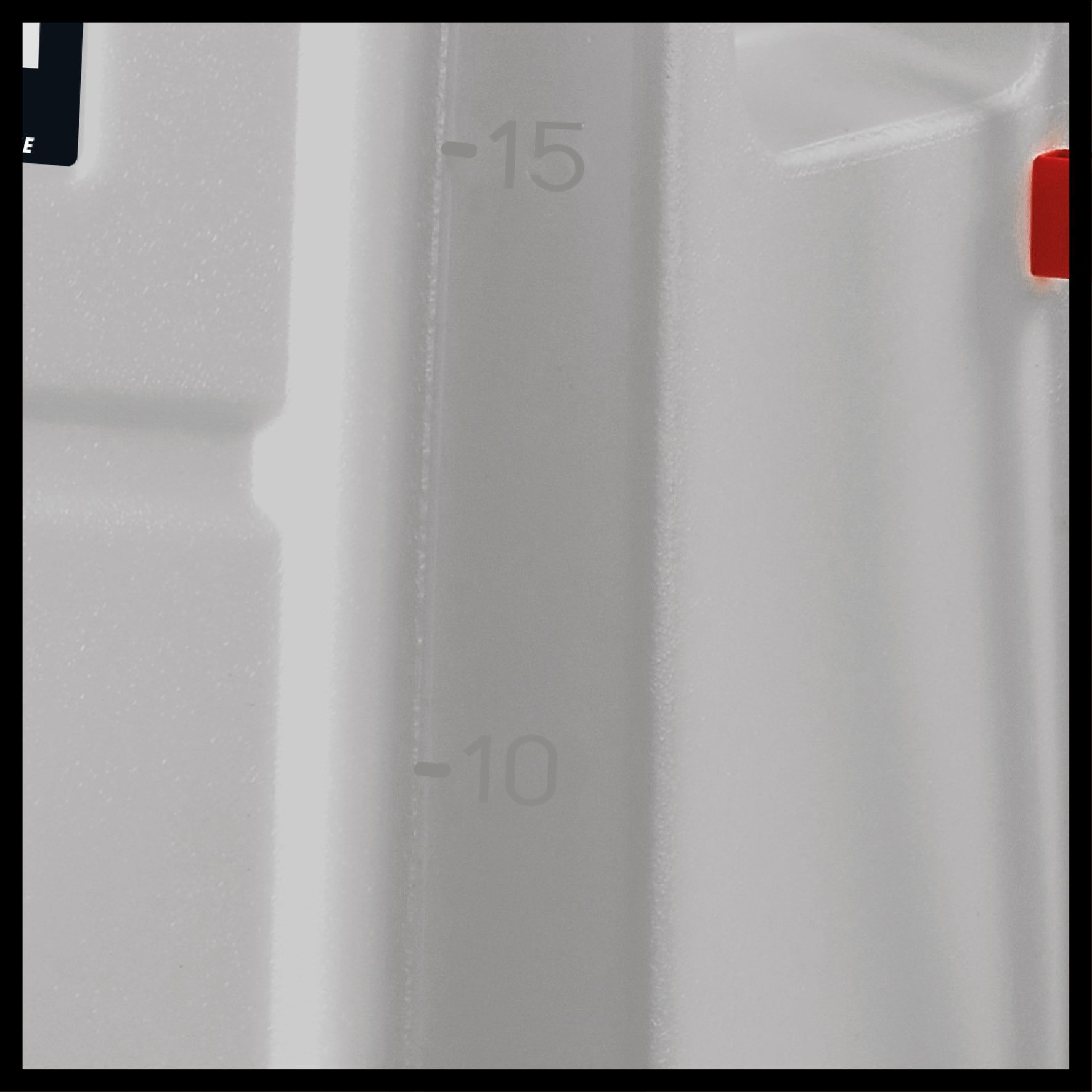 Primo piano di un contenitore bianco con segni di misurazione. Elemento rosso sul lato. Sfondo scuro.
