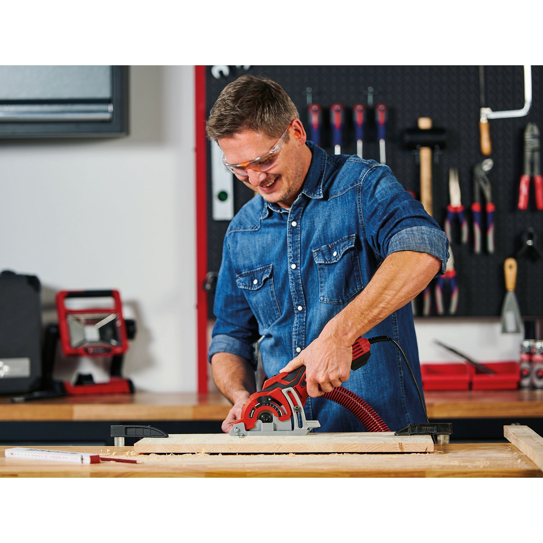 Mężczyzna używa czerwonej piły tarczowej na drewnie, okulary ochronne w warsztacie.