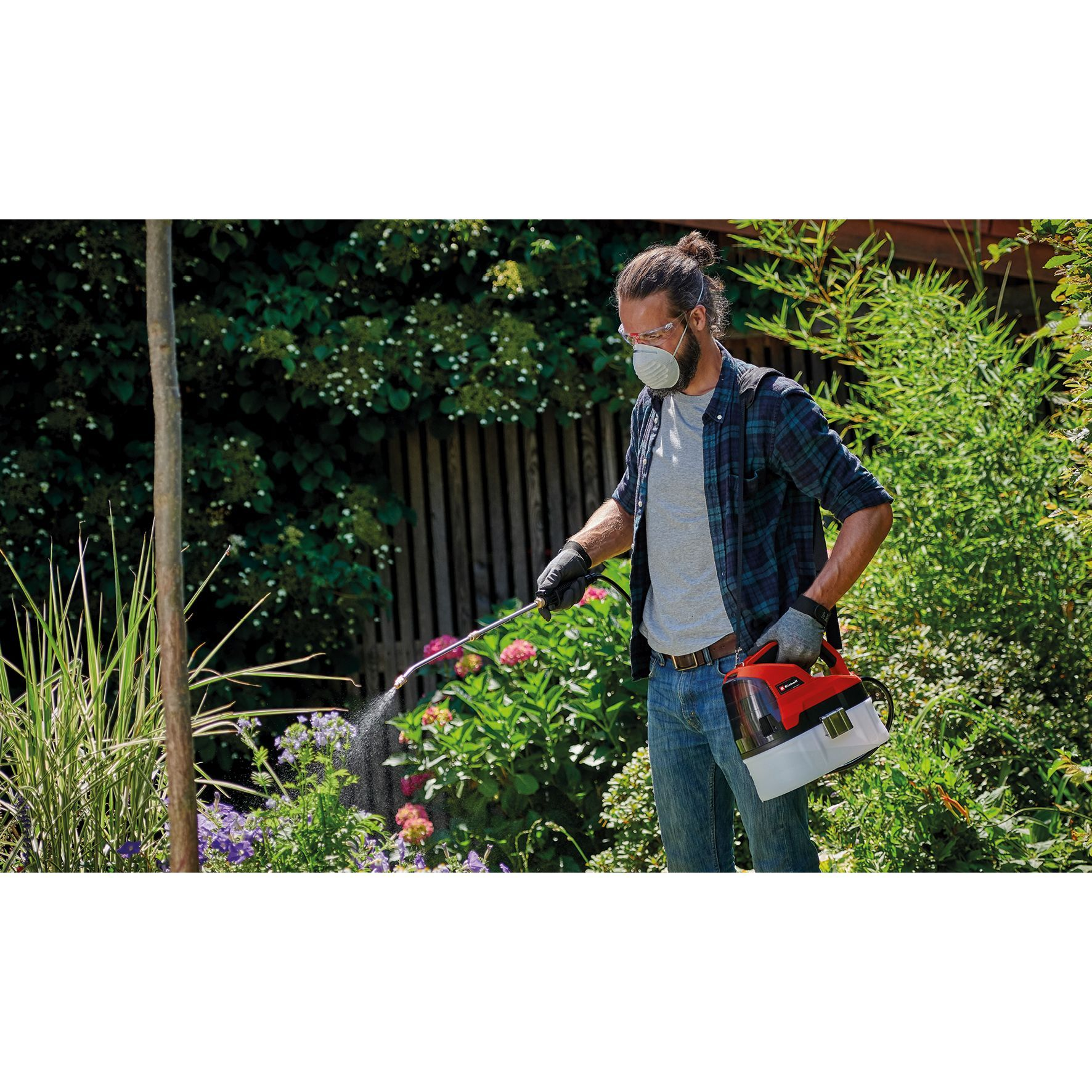 Mann im Garten, der Pflanzen mit Pestiziden besprüht. Er trägt eine Maske und Handschuhe.