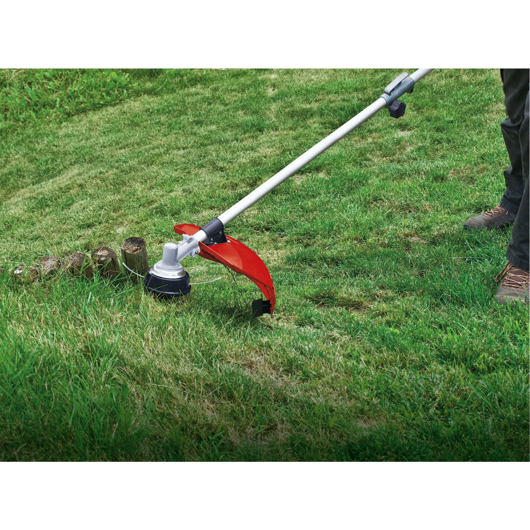 Eine Person benutzt einen rot-schwarzen Fadentrimmer, um Gras in einem Garten zu schneiden.