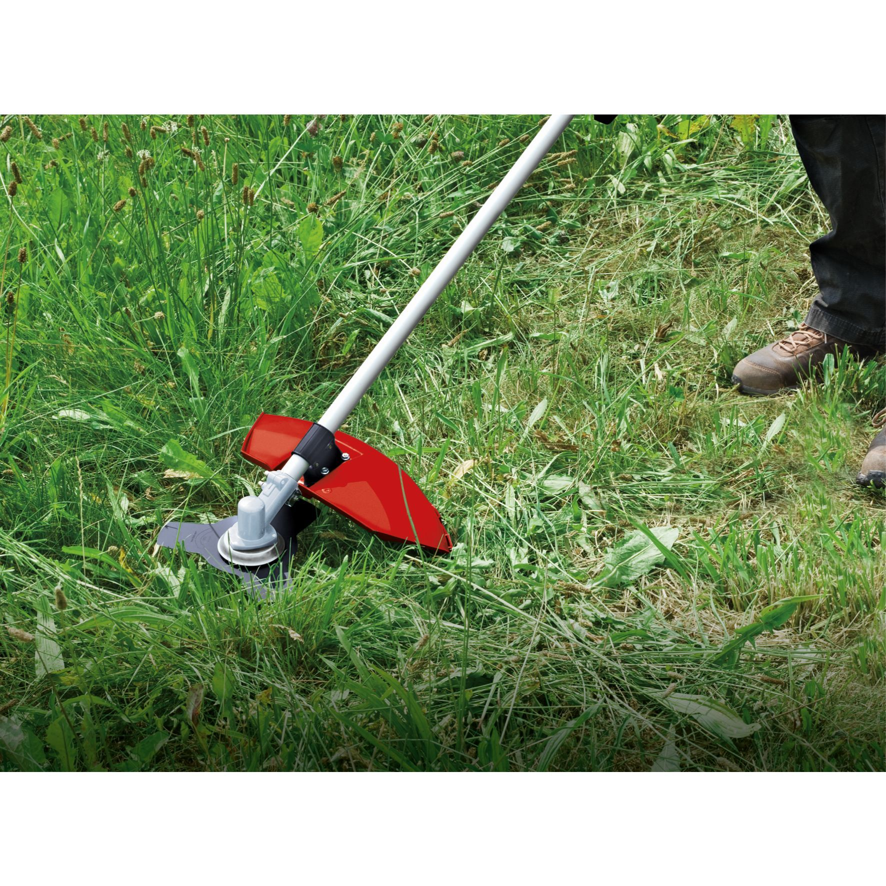 Person verwendet einen roten Rasentrimmer in einem grasbewachsenen Bereich. Sie tragen braune Schuhe.