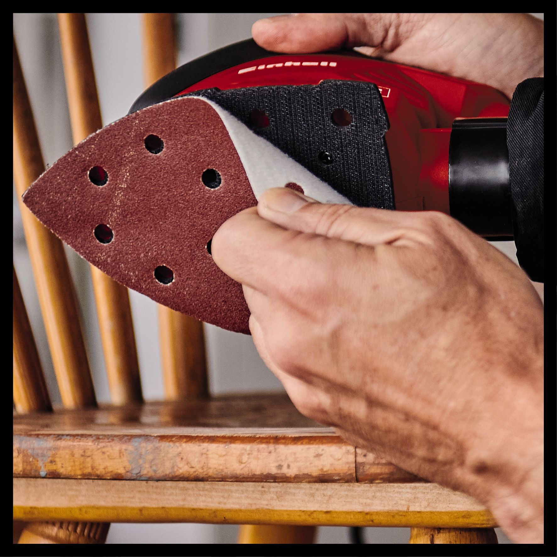 Osoba używa czerwonej szlifierki na drewnianym krześle.