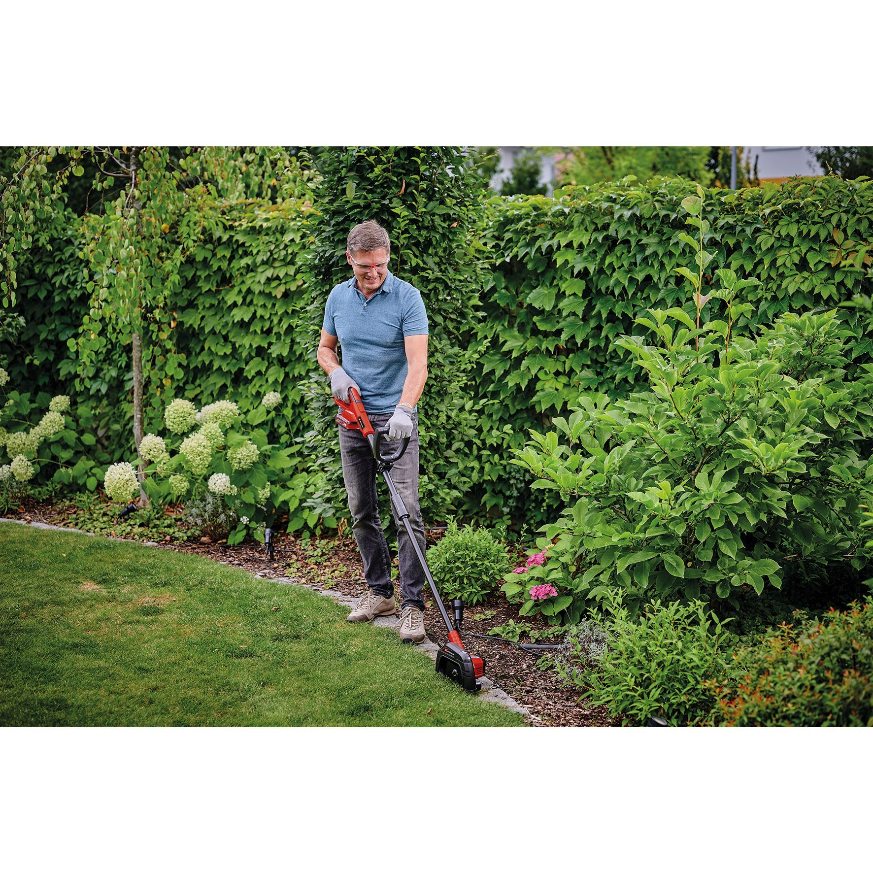 Un uomo taglia il bordo dell'erba in un giardino, usando un trimmer elettrico.