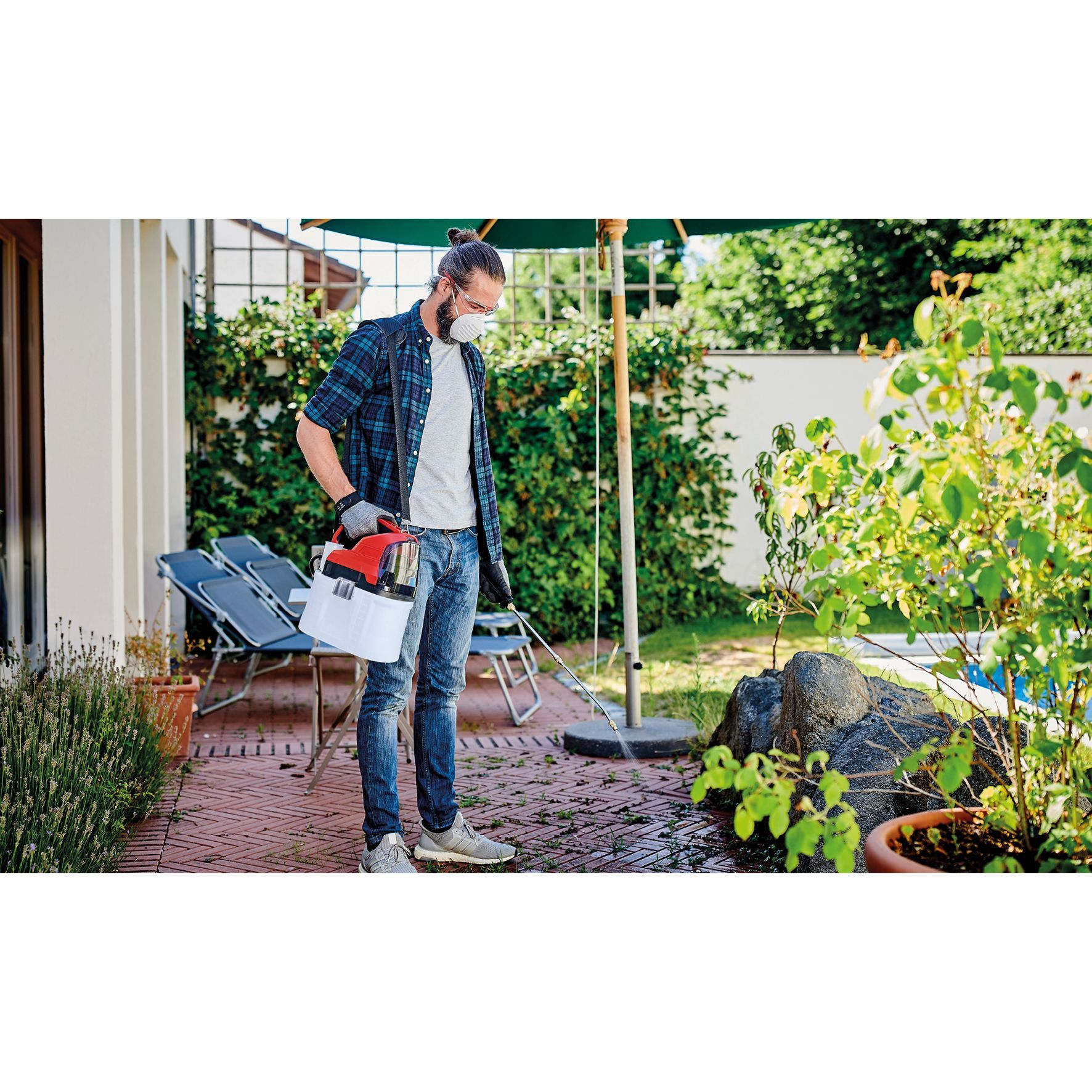 Mann besprüht Pflanzen in einem Garten mit einem Sprühgerät und Maske.