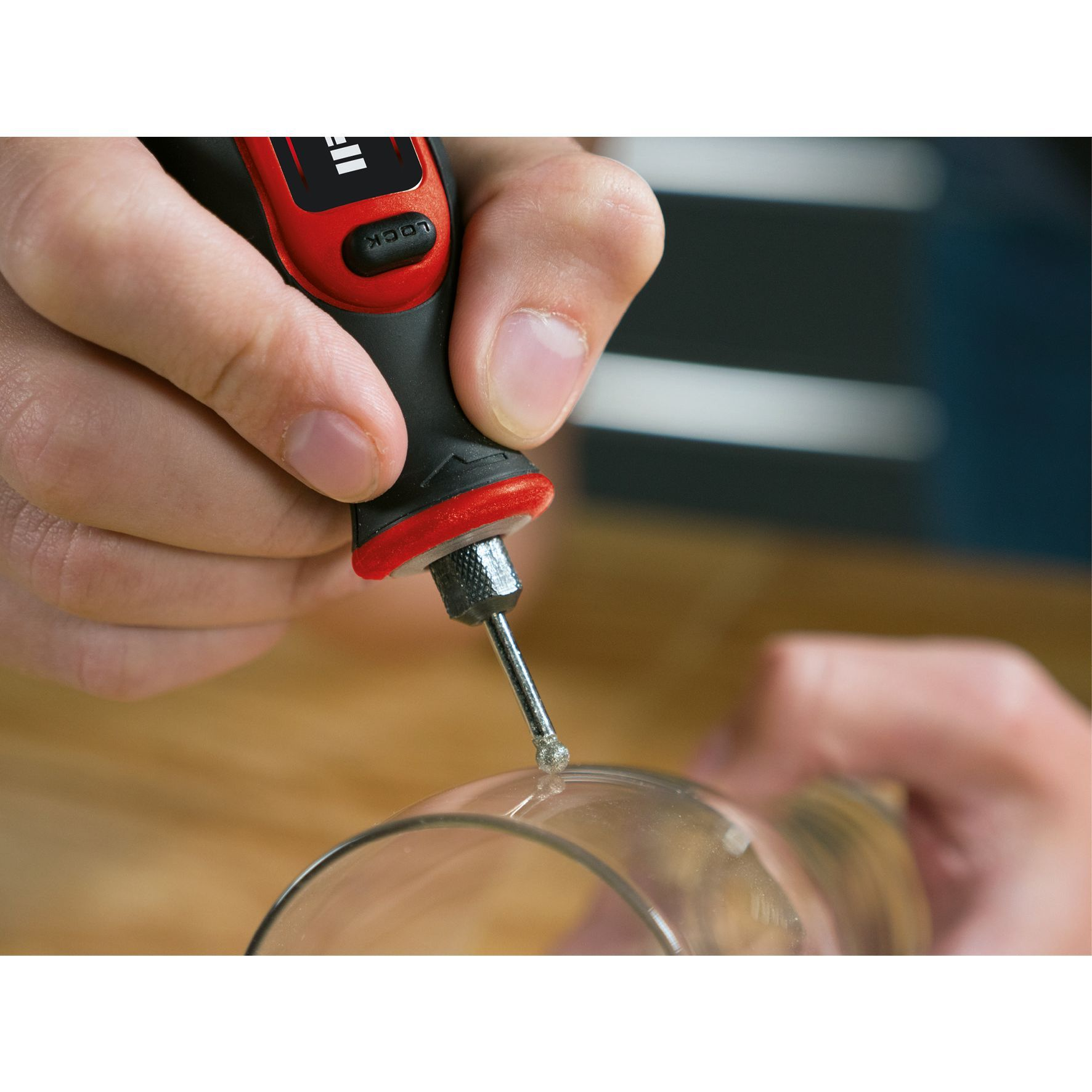 Eine Hand benutzt ein Rotationswerkzeug auf Glas. Das Werkzeug ist rot und schwarz, das Glas ist klar.