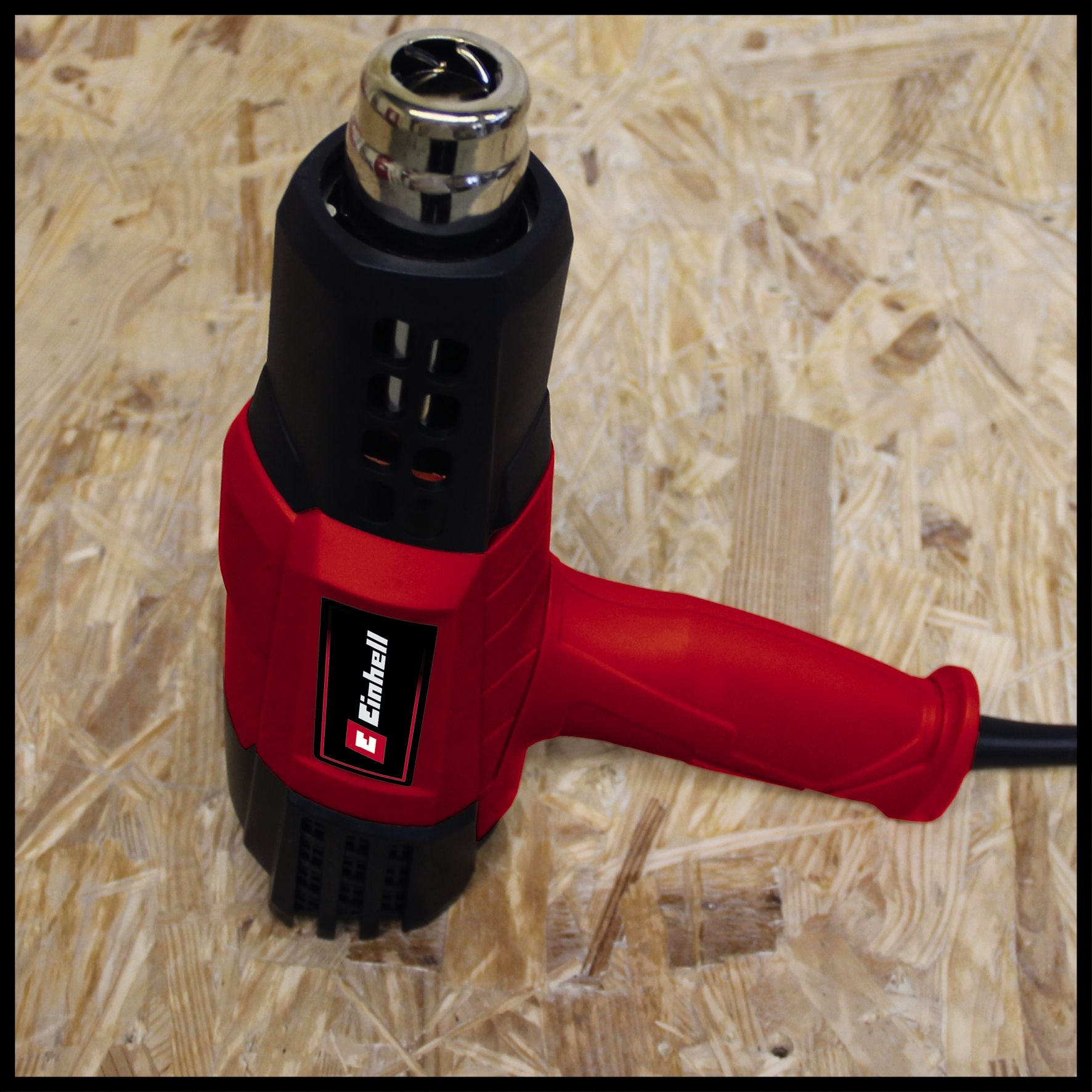 Pistolet thermique rouge et noir sur une surface en bois. La marque 'Einhell' est visible.