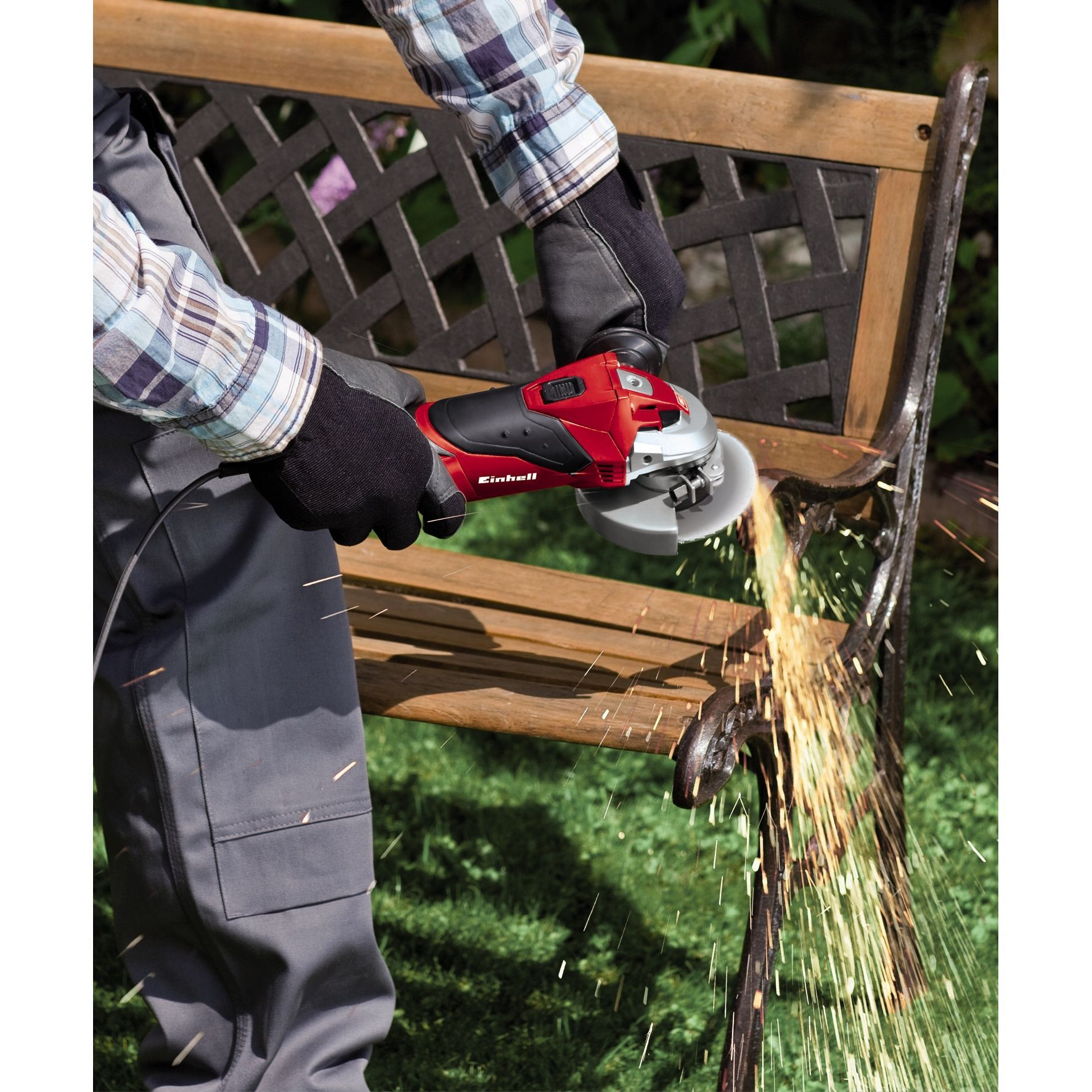 Osoba szlifuje drewnianą ławkę czerwoną szlifierką kątową, lecą iskry. Widoczne rękawice i koszula w kratę.