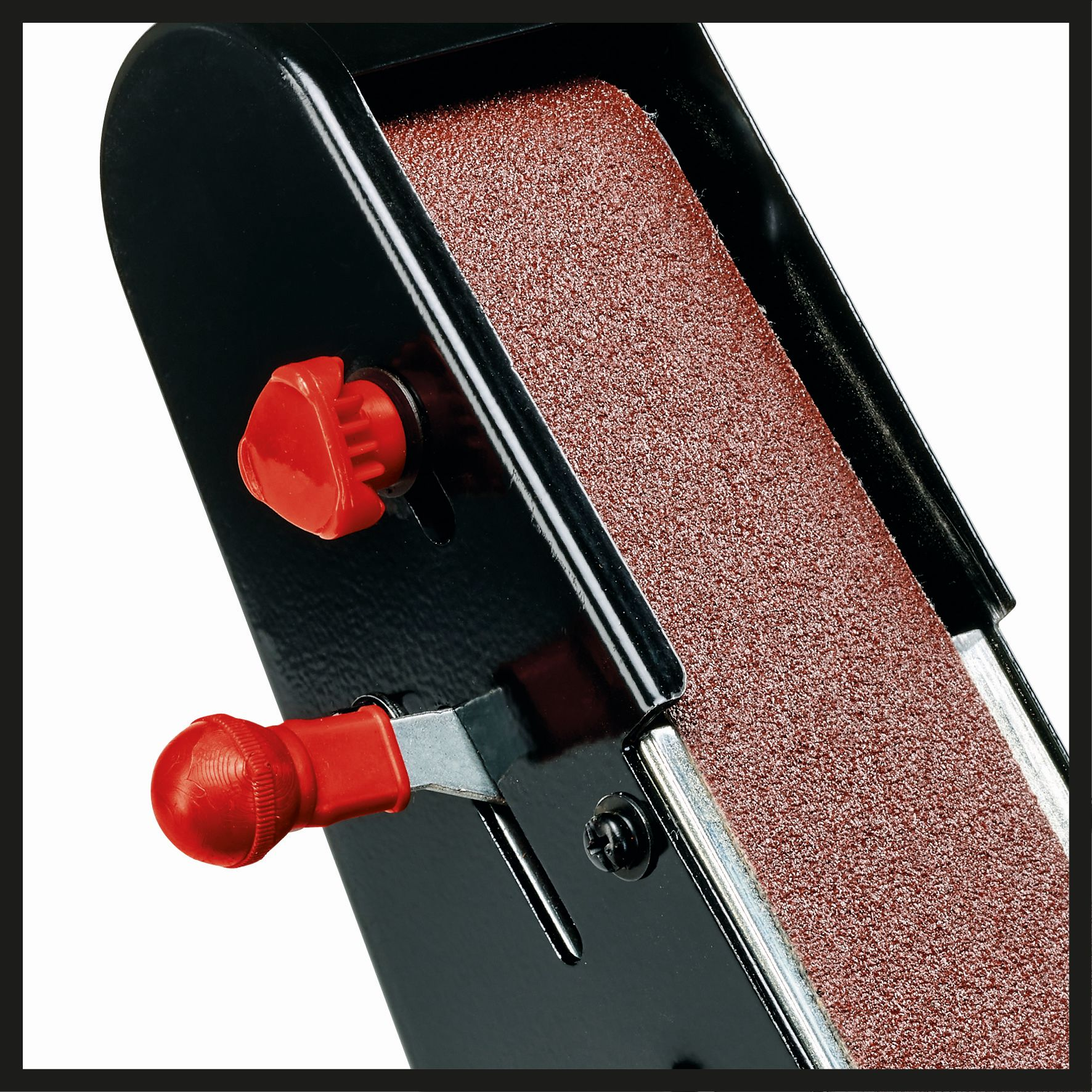 Zbliżenie szlifierki taśmowej. Widoczne czerwone pokrętło i taśma szlifierska. Czarno-białe.