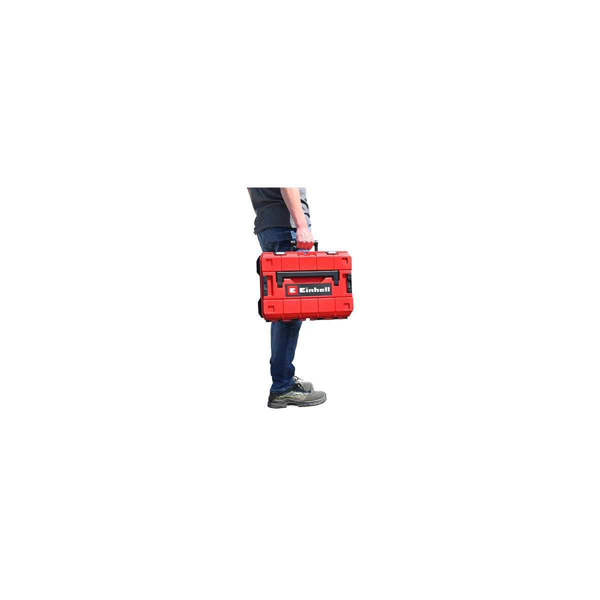 Mann, der eine rote Werkzeugkiste trägt. Er trägt Jeans, ein dunkles Hemd und graue Schuhe.