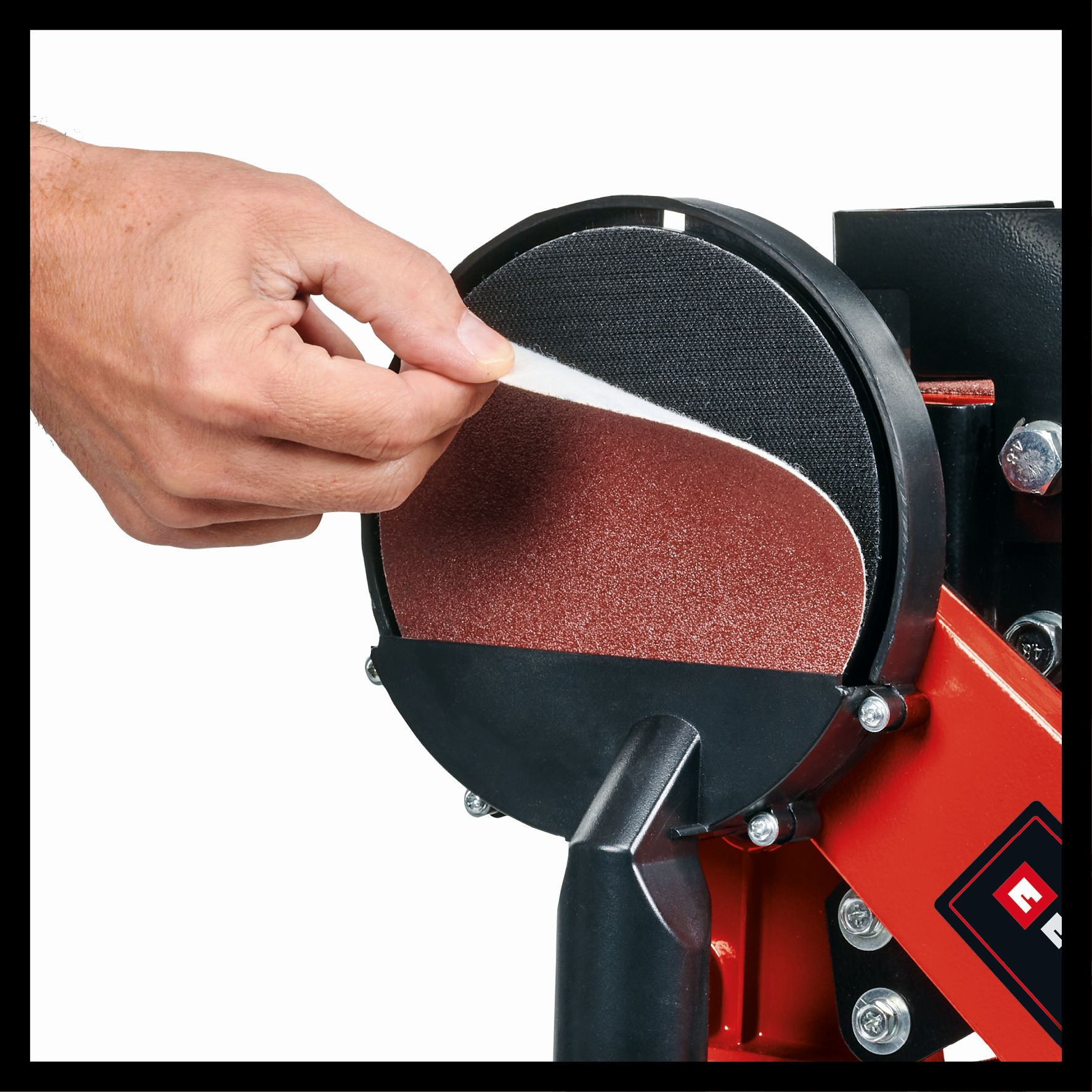 Une main retire un disque de ponçage d'une ponceuse d'établi rouge et noire.