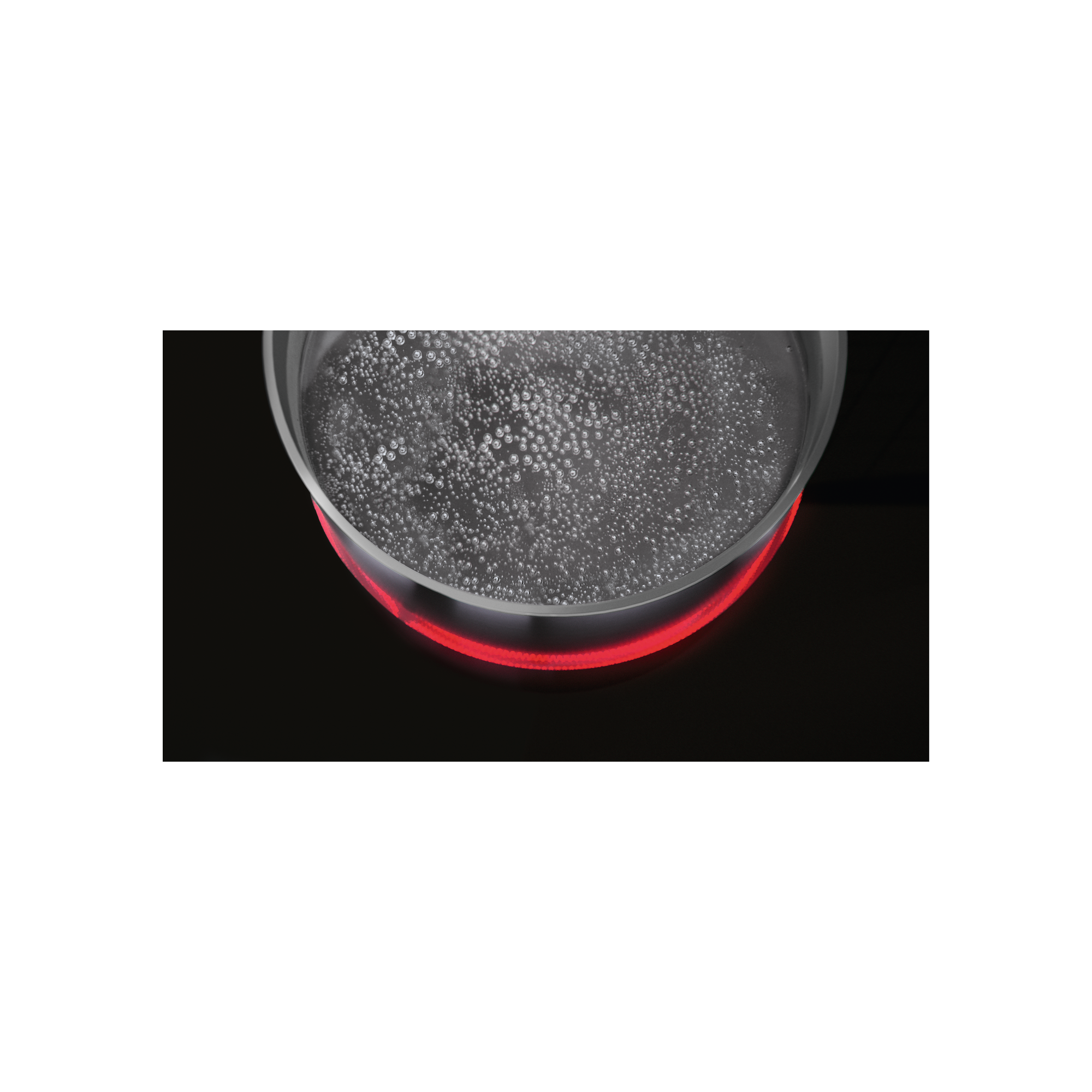 Zbliżenie wrzącej wody w przezroczystym szklanym garnku na czarnej płycie grzejnej.