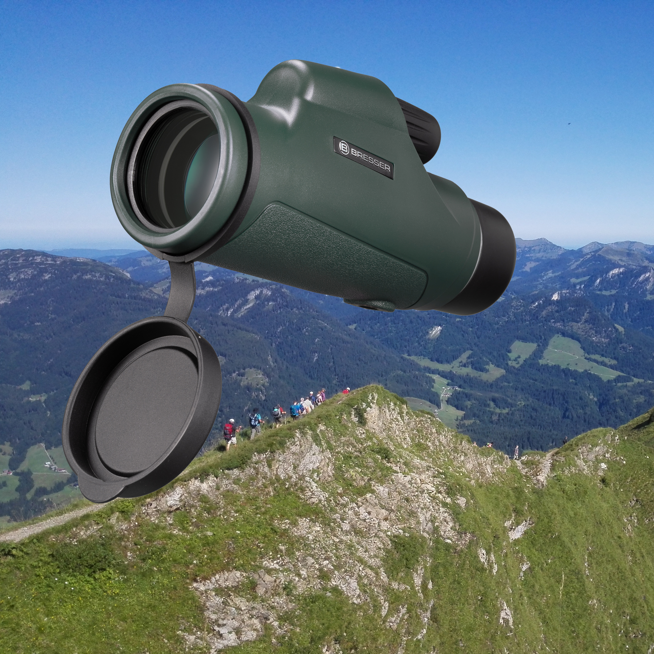 Grünes Monokular mit geöffneter Objektivkappe auf einem Berggipfel mit Wanderern im Hintergrund.