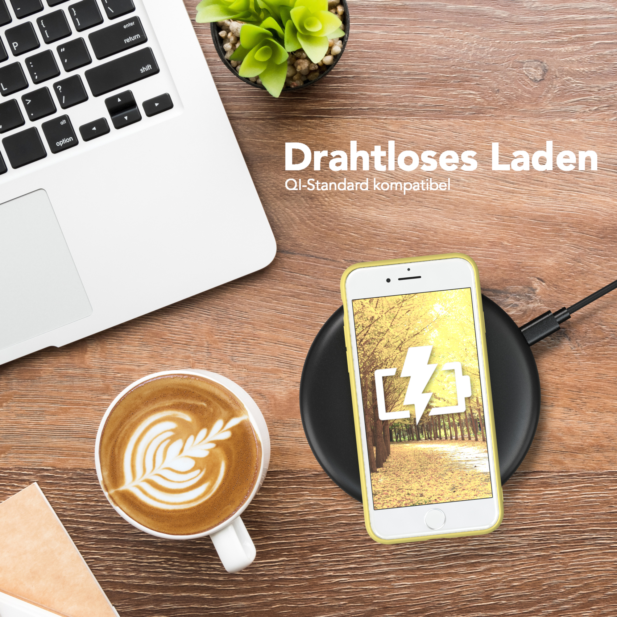 Ein Telefon, das auf einem schwarzen Pad geladen wird. Daneben eine Kaffeetasse und ein Laptop.