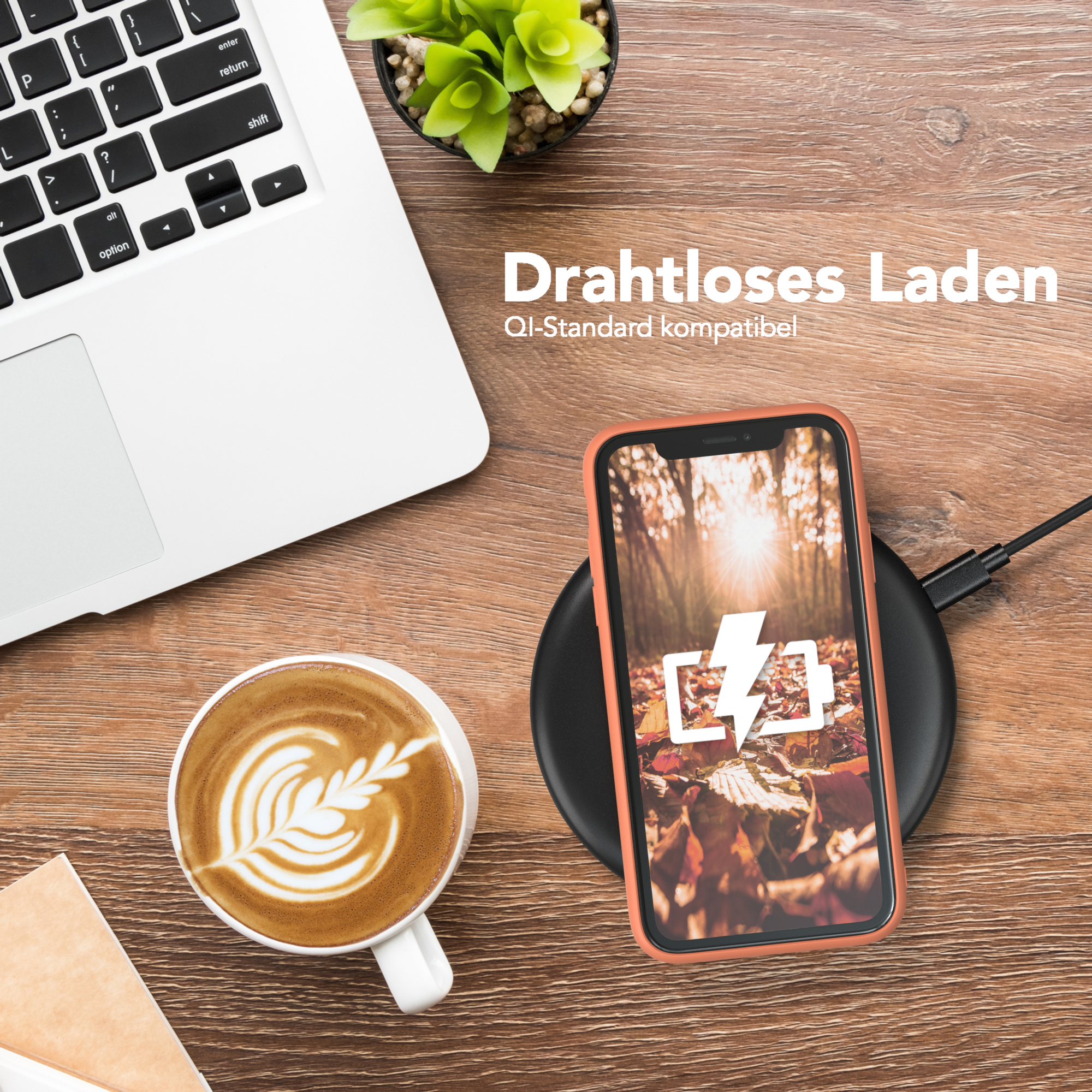 Telefon mit orangefarbener Hülle auf kabellosem Ladegerät, neben Laptop und Kaffee mit Latte Art.