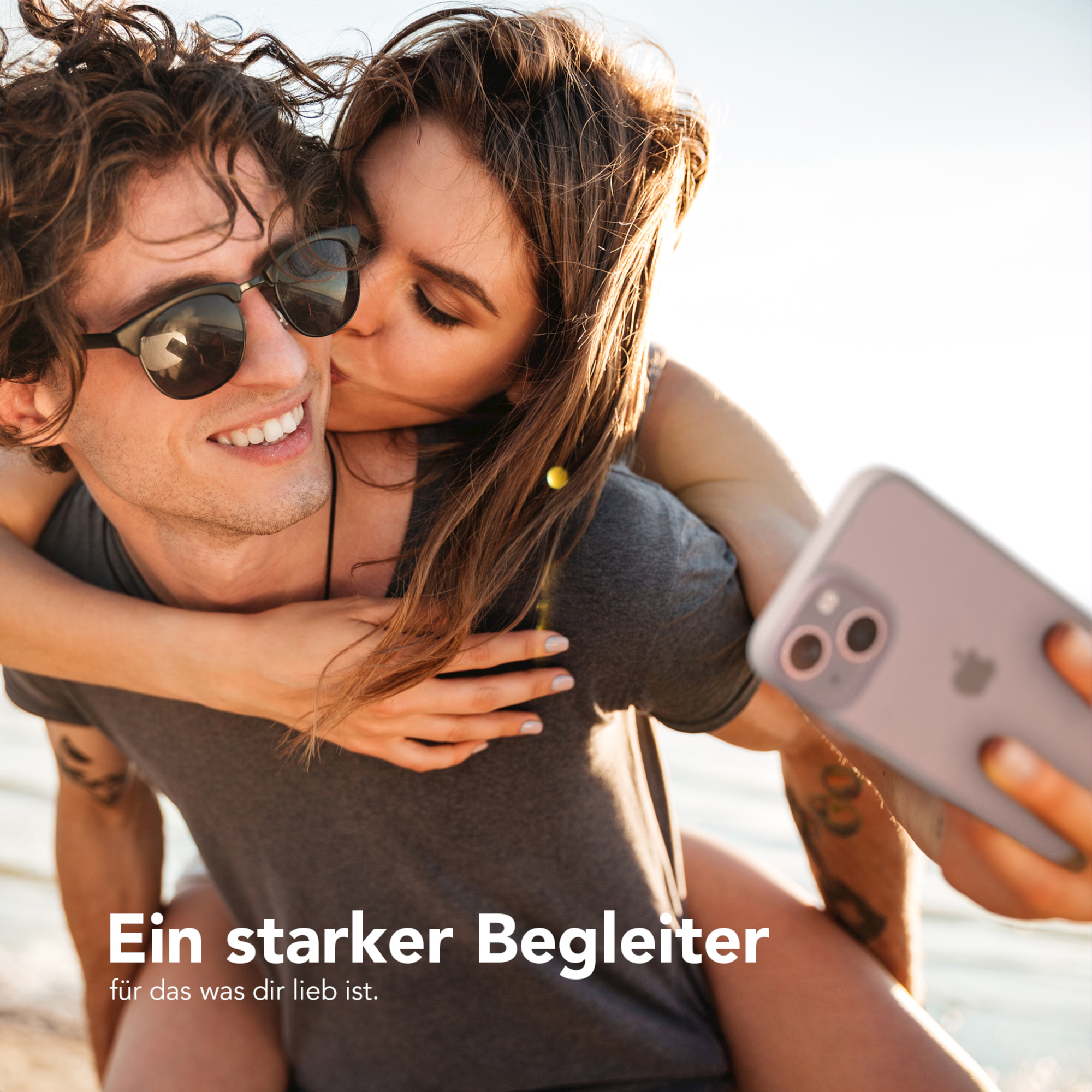 Paar macht Selfie. Frau küsst Mann. Er hält das Telefon mit klarer Hülle.