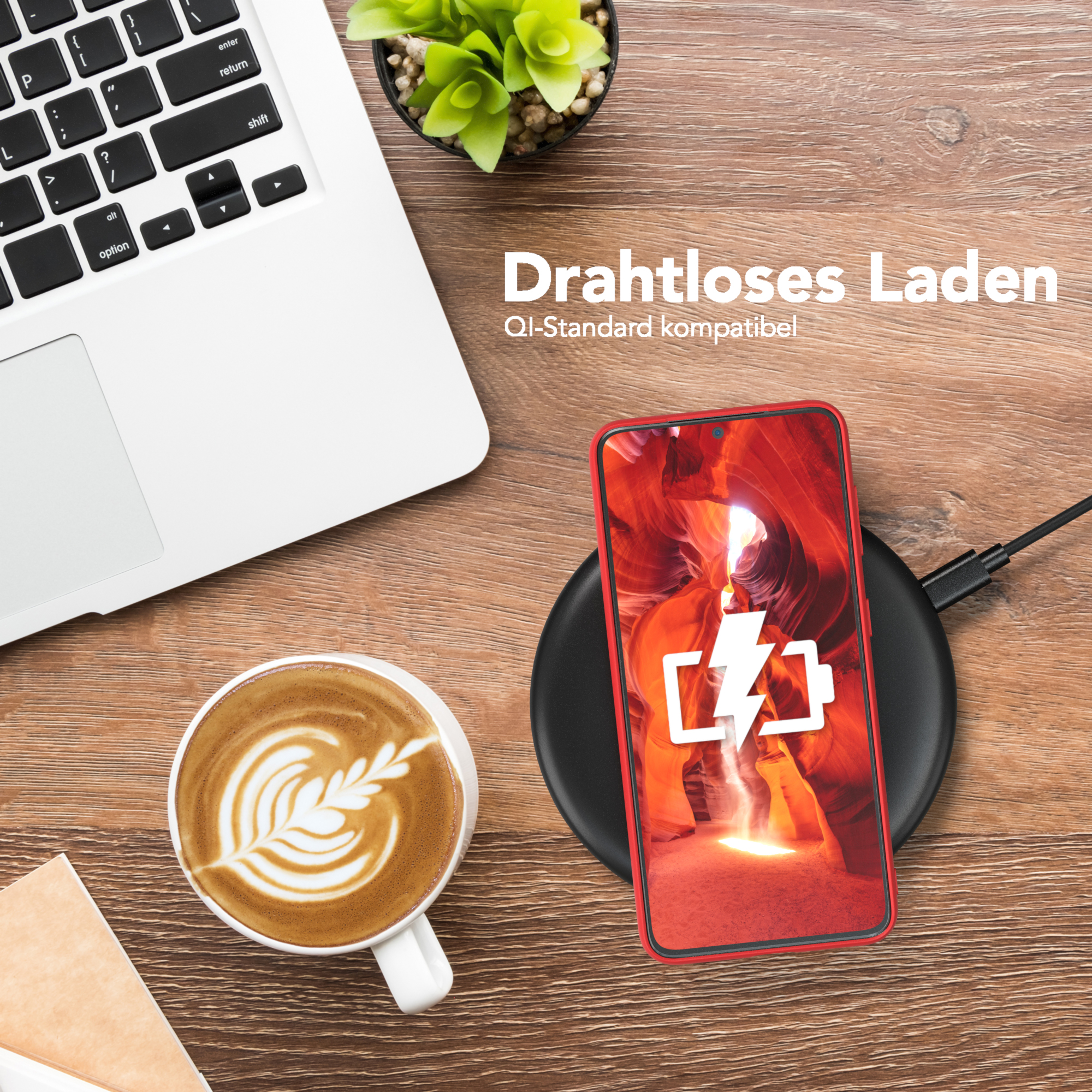 Ein Telefon wird drahtlos auf einem schwarzen Pad aufgeladen. Eine Kaffeetasse und ein Laptop stehen auf einem Holztisch.