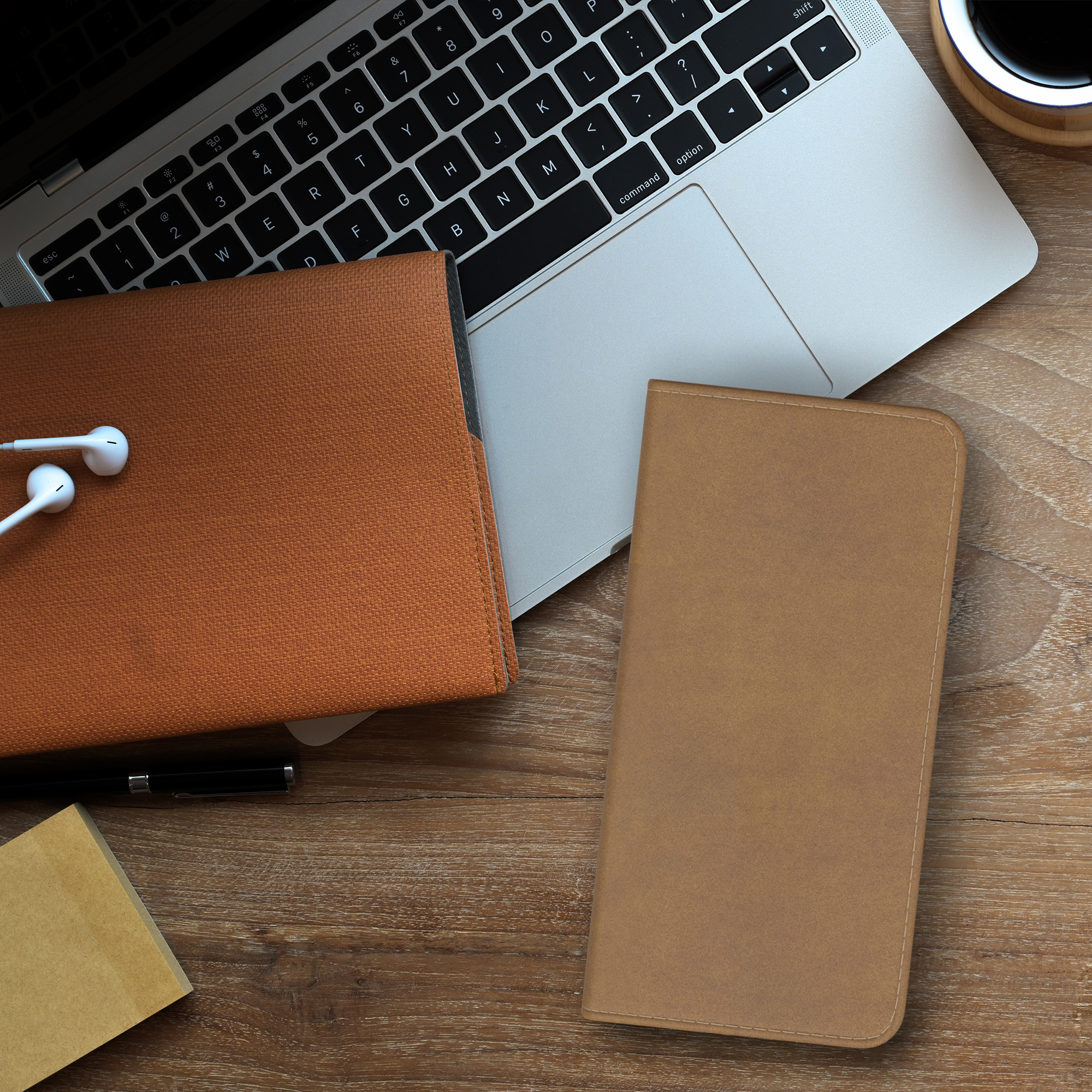 Laptop, Notizblock, Stift und Kopfhörer auf einem Holzschreibtisch mit einer Kaffeetasse.