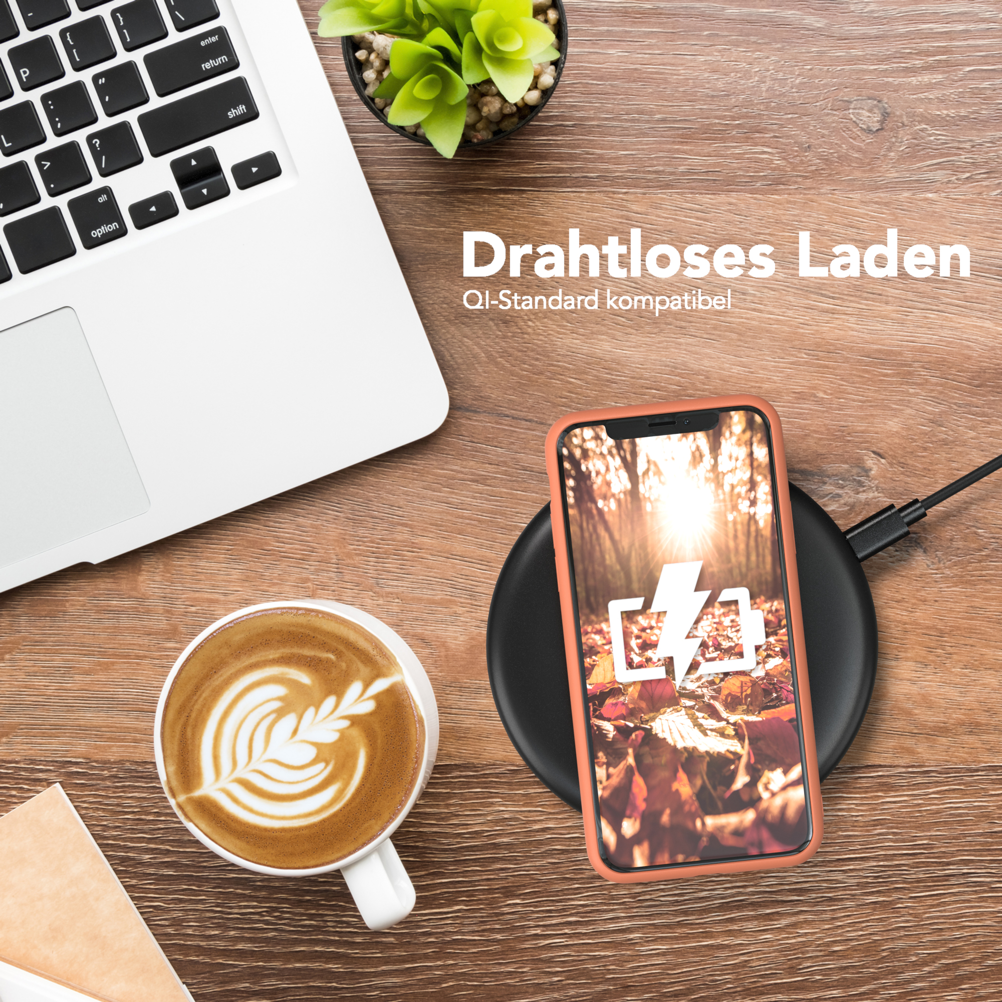 Ein Telefon mit orangefarbener Hülle liegt auf einem kabellosen Ladegerät. Ein Laptop, Kaffee und eine kleine Pflanze befinden sich ebenfalls auf dem Schreibtisch.