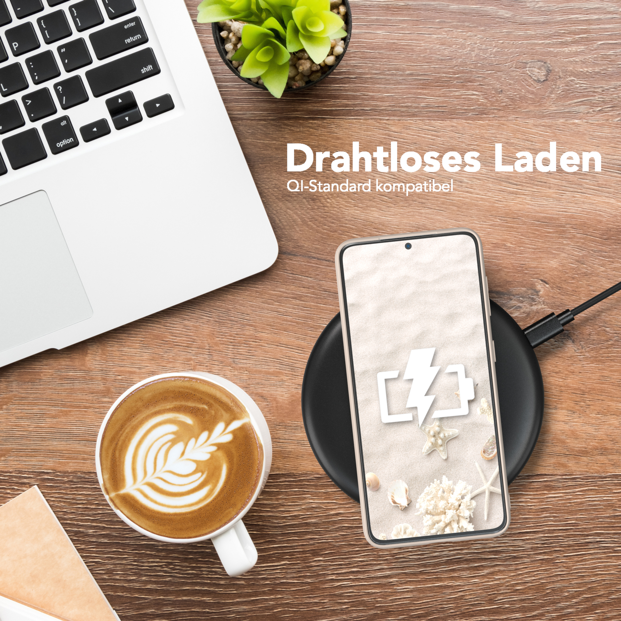 Ein Telefon liegt auf einem kabellosen Ladepad neben einem Laptop und einer Kaffeetasse mit Latte Art.