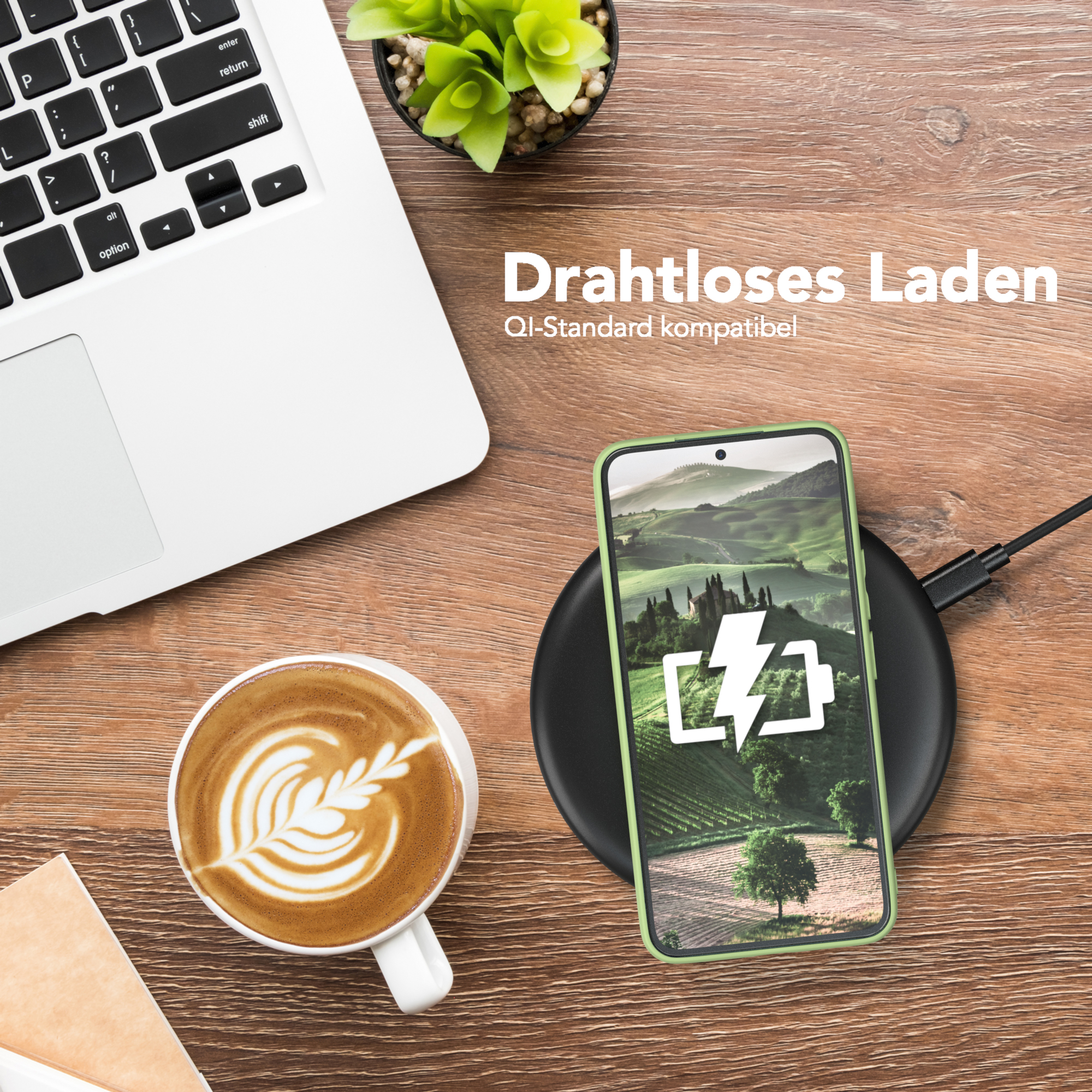 Ein Handy auf einem kabellosen Ladegerät neben einem Laptop, einer Kaffeetasse und einer kleinen Pflanze auf einem Holztisch.