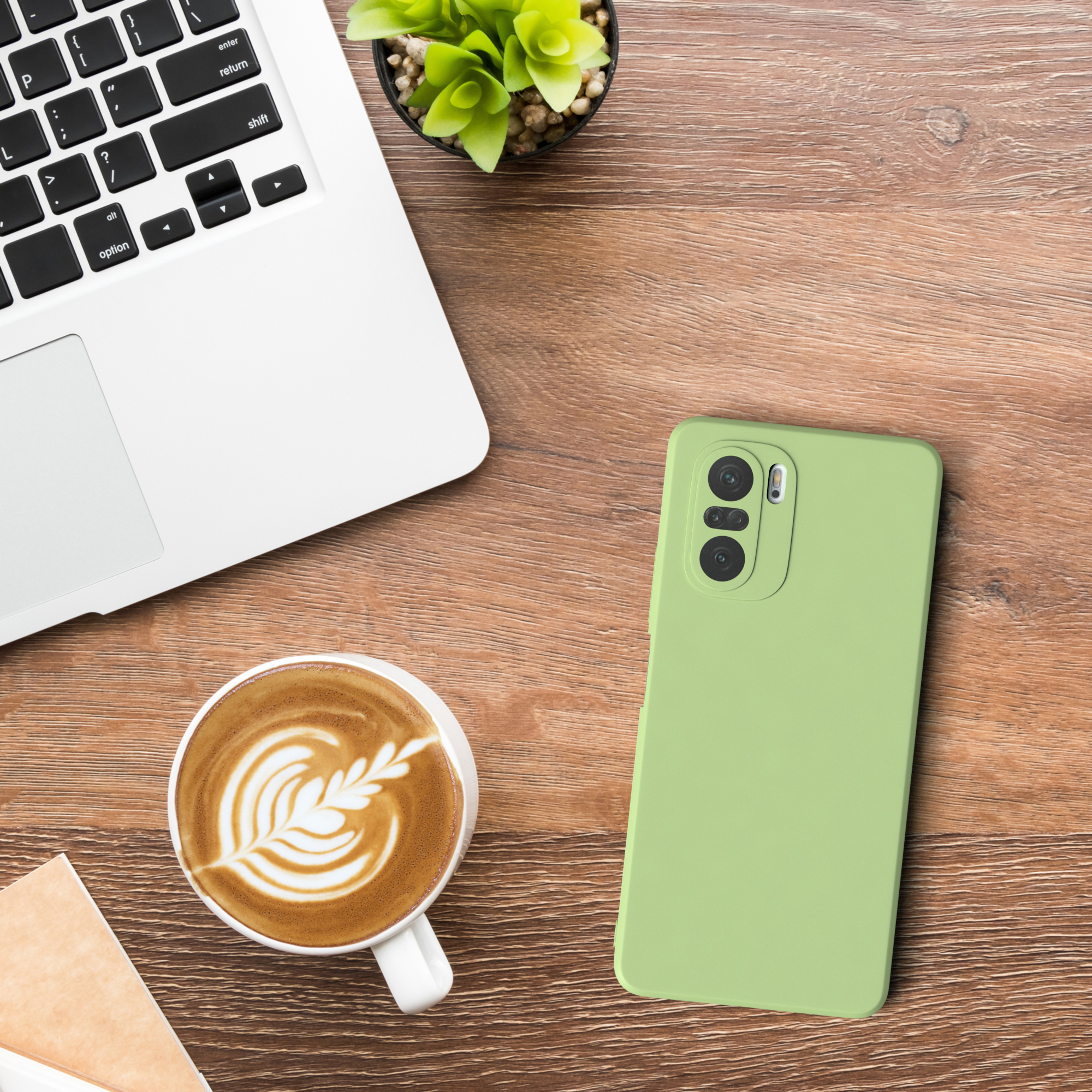 Ein Laptop, eine Tasse Kaffee und ein Telefon in einer grünen Hülle liegen auf einem Holztisch.