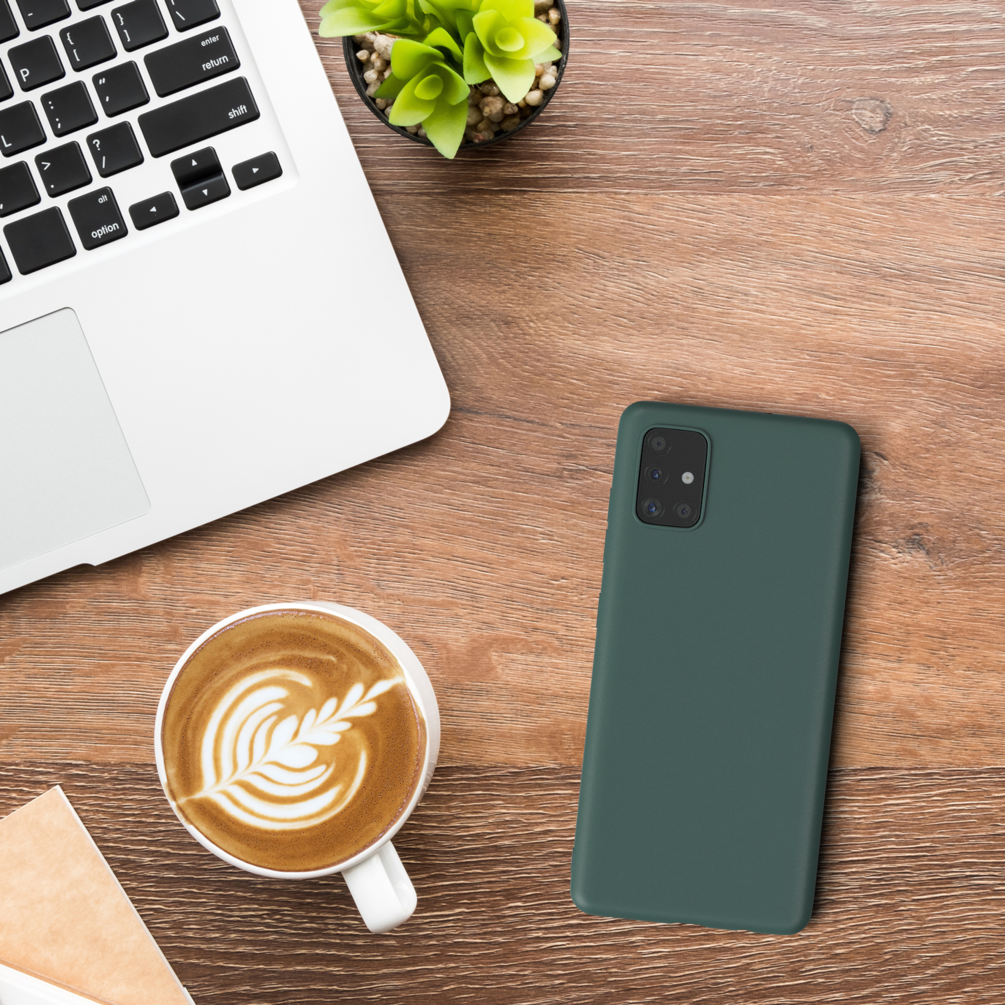 Draufsicht auf einen Schreibtisch mit Laptop, Kaffee, Handyhülle und Pflanze. Die Hülle ist grün.